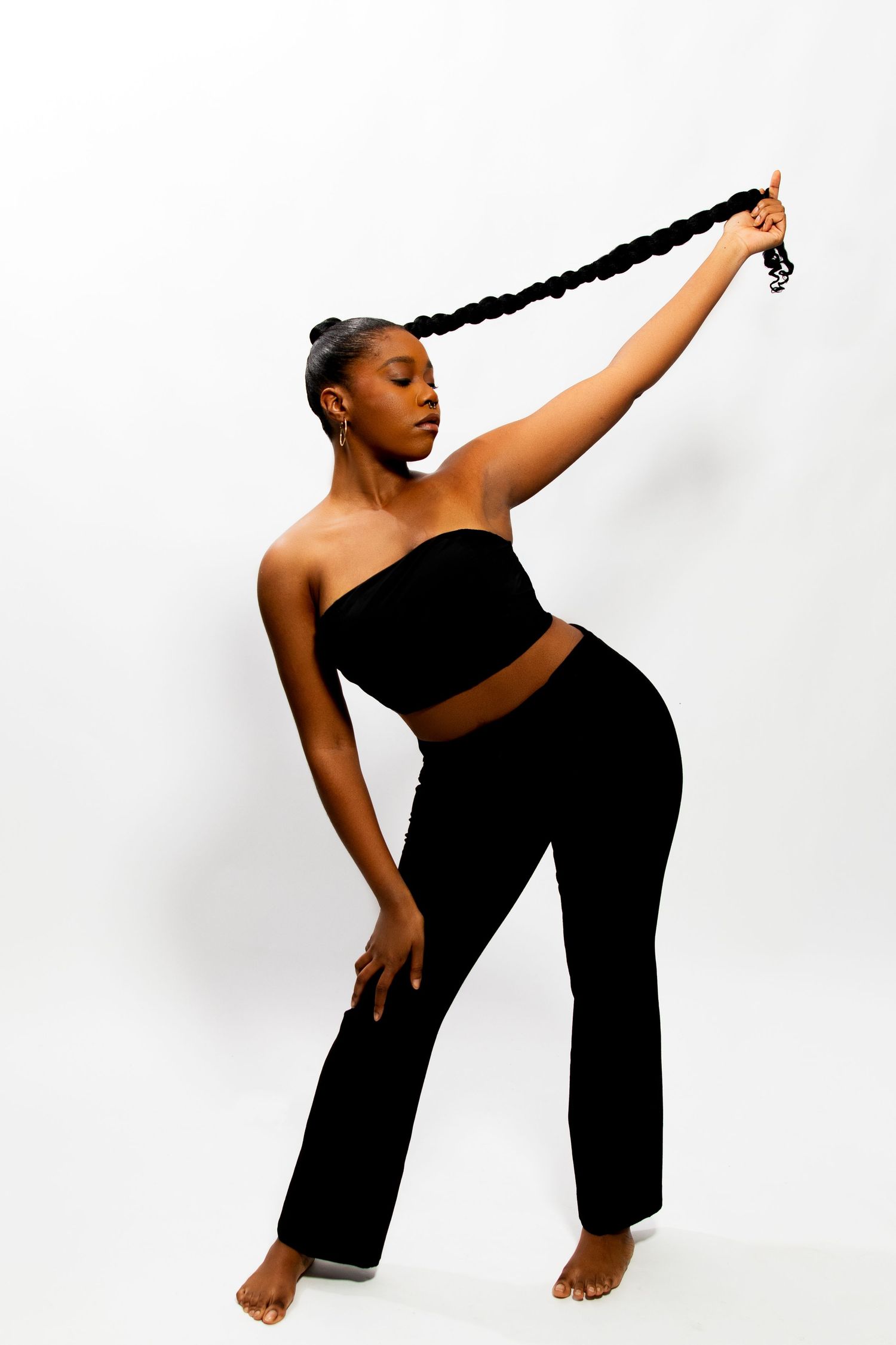 Woman in black outfit lifting long braided hair extension overhead gracefully.