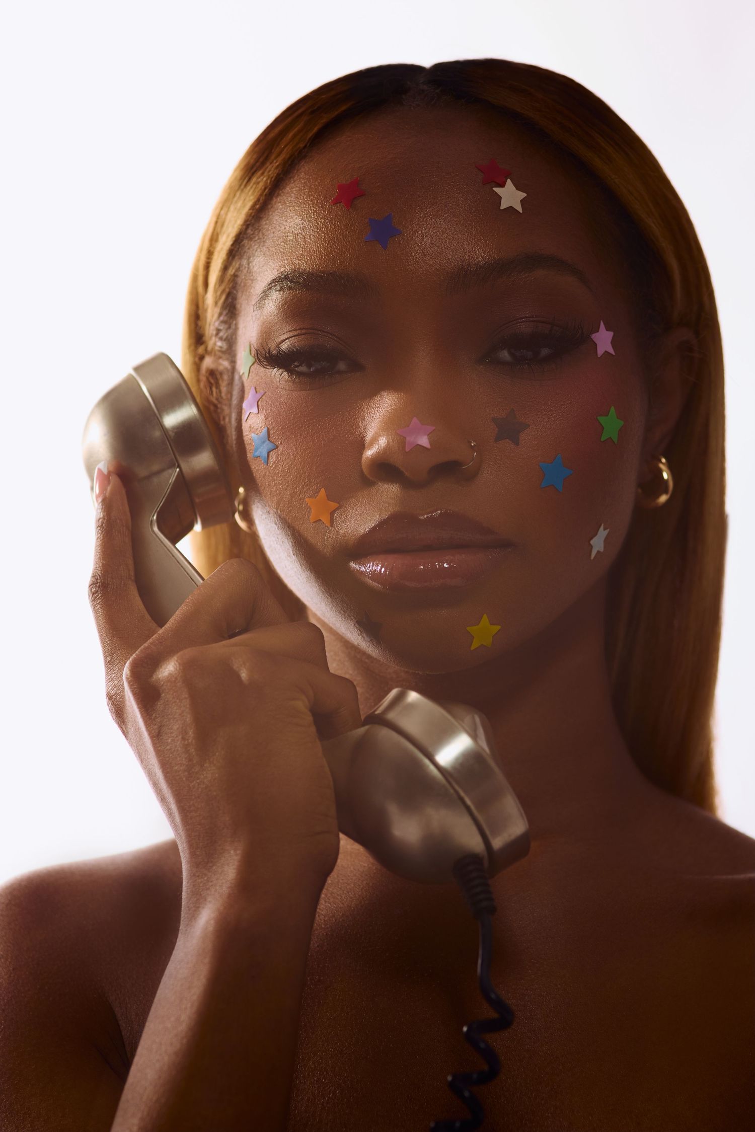 Stylish Black woman with colorful star confetti stickers on face posing with retro silver phone handset.