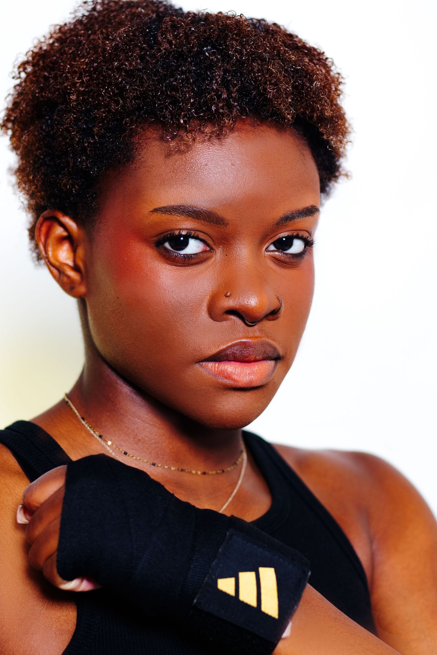 Close-up portrait of a young Black female boxer with hand wraps and gold necklace in Adidas sportswear.