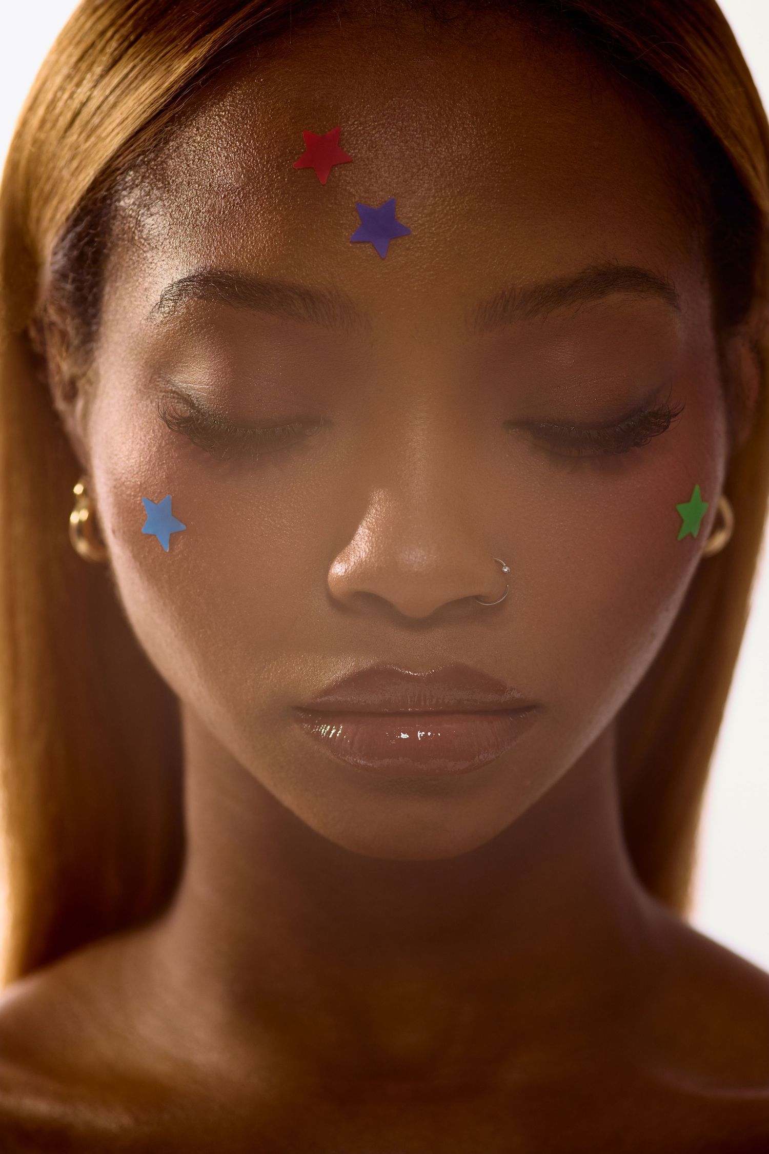 Portrait of woman with eyes closed wearing colorful star Starface pimple patches on forehead and cheeks.