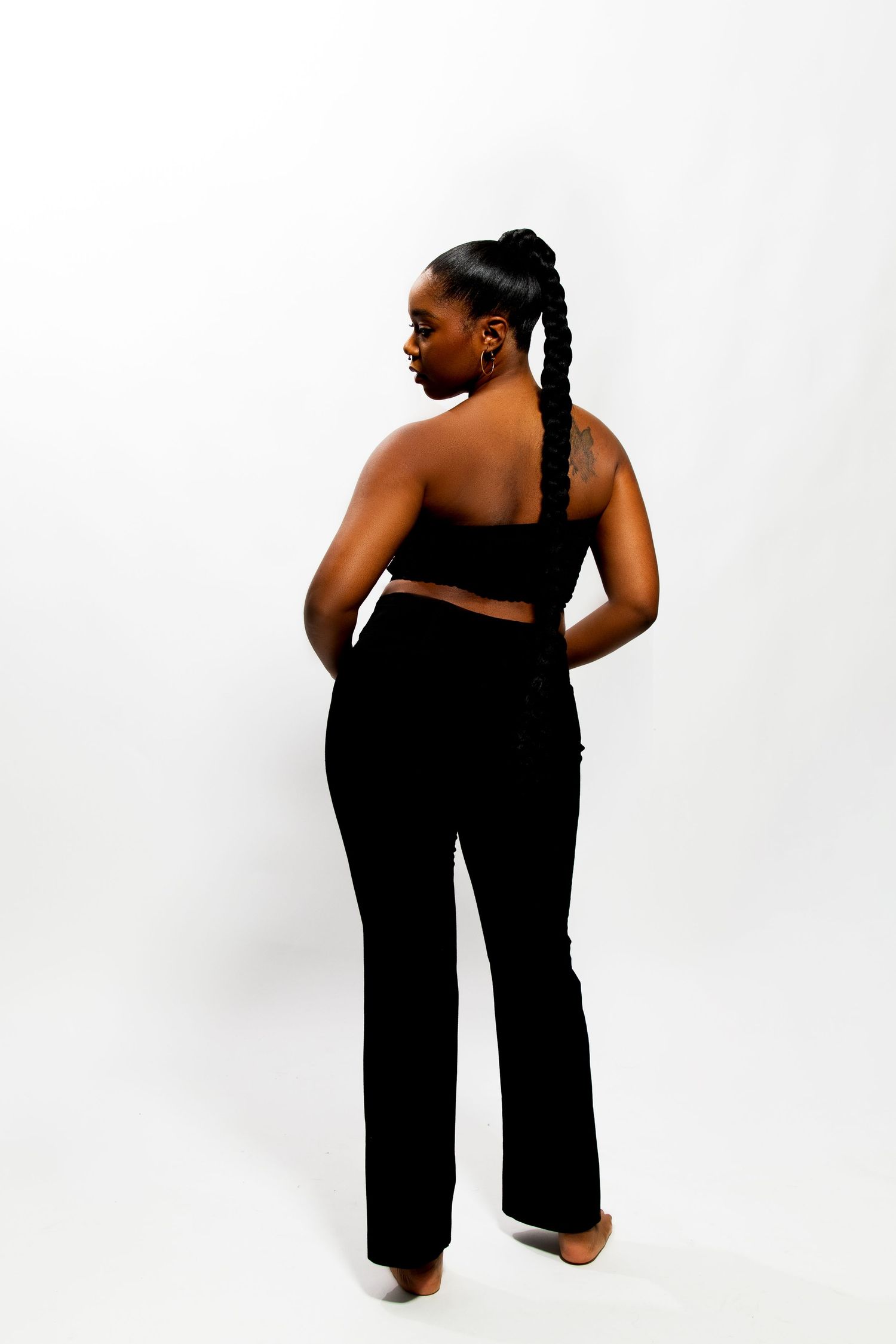 Rear view of Black woman in black bandeau top and flared pants with braided ponytail.