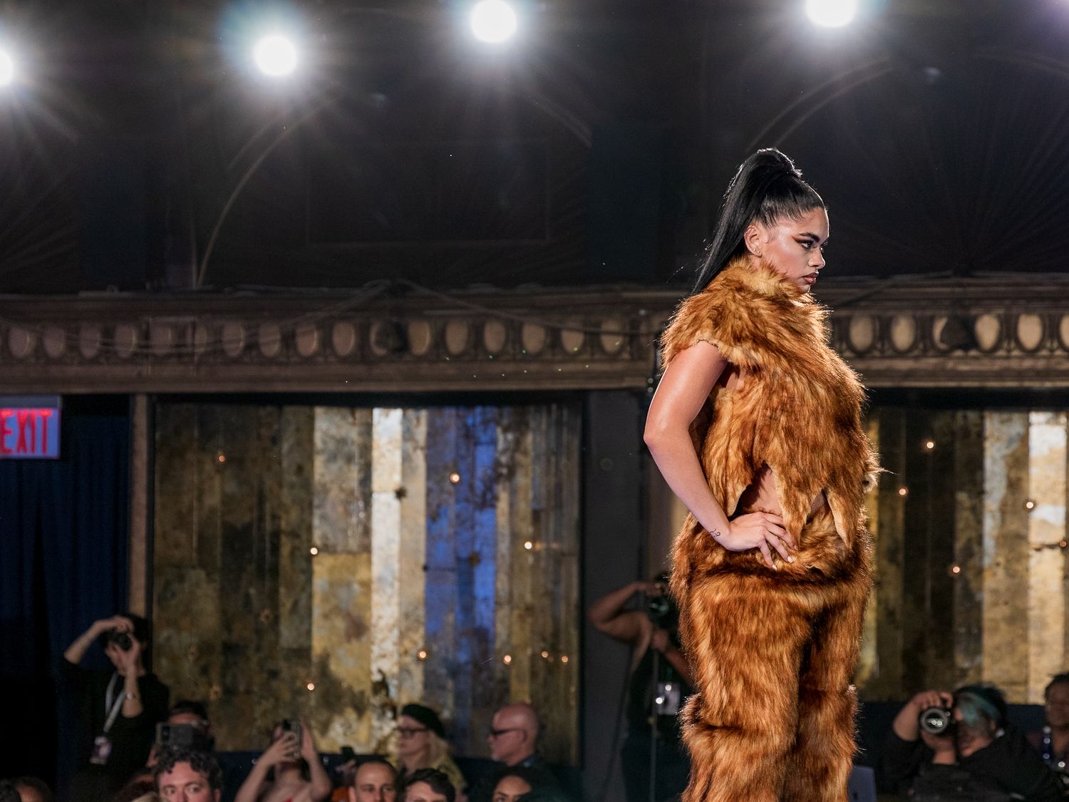 Model poses confidently on runway in luxurious golden brown faux fur outfit at fashion show.