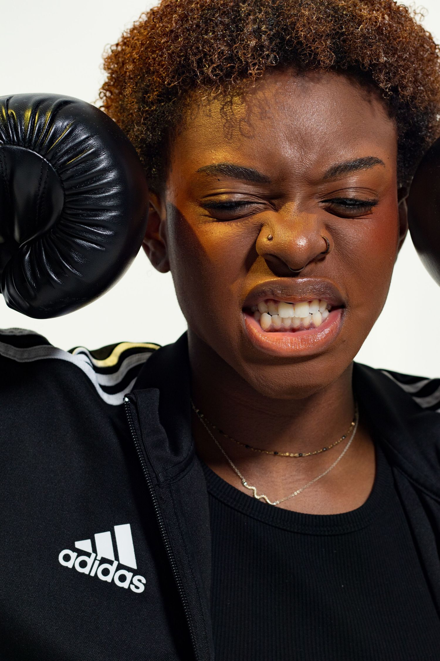 Fierce young Black female boxer grimacing with black Adidas boxing glove raised beside her face.