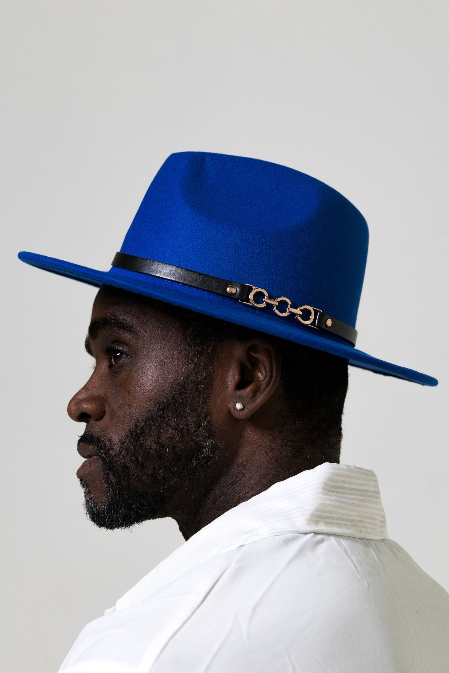 Side profile of Black man wearing bold royal blue wide-brim felt hat with leather band.