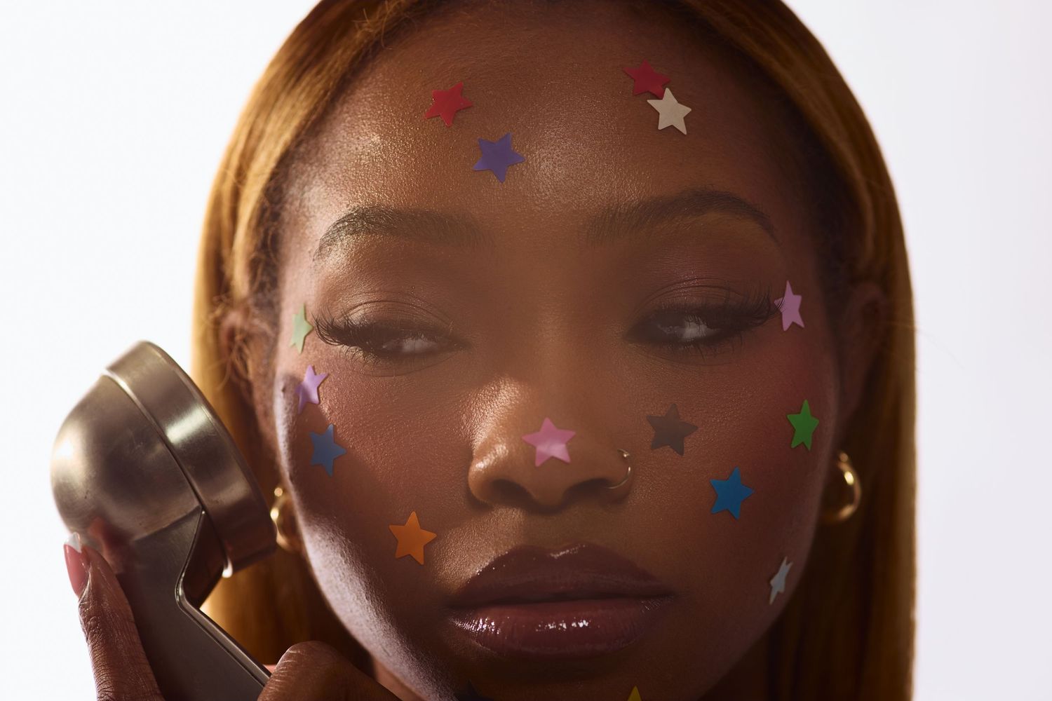 Close-up of Black woman with colorful star stickers on face holding vintage telephone handset to her ear.