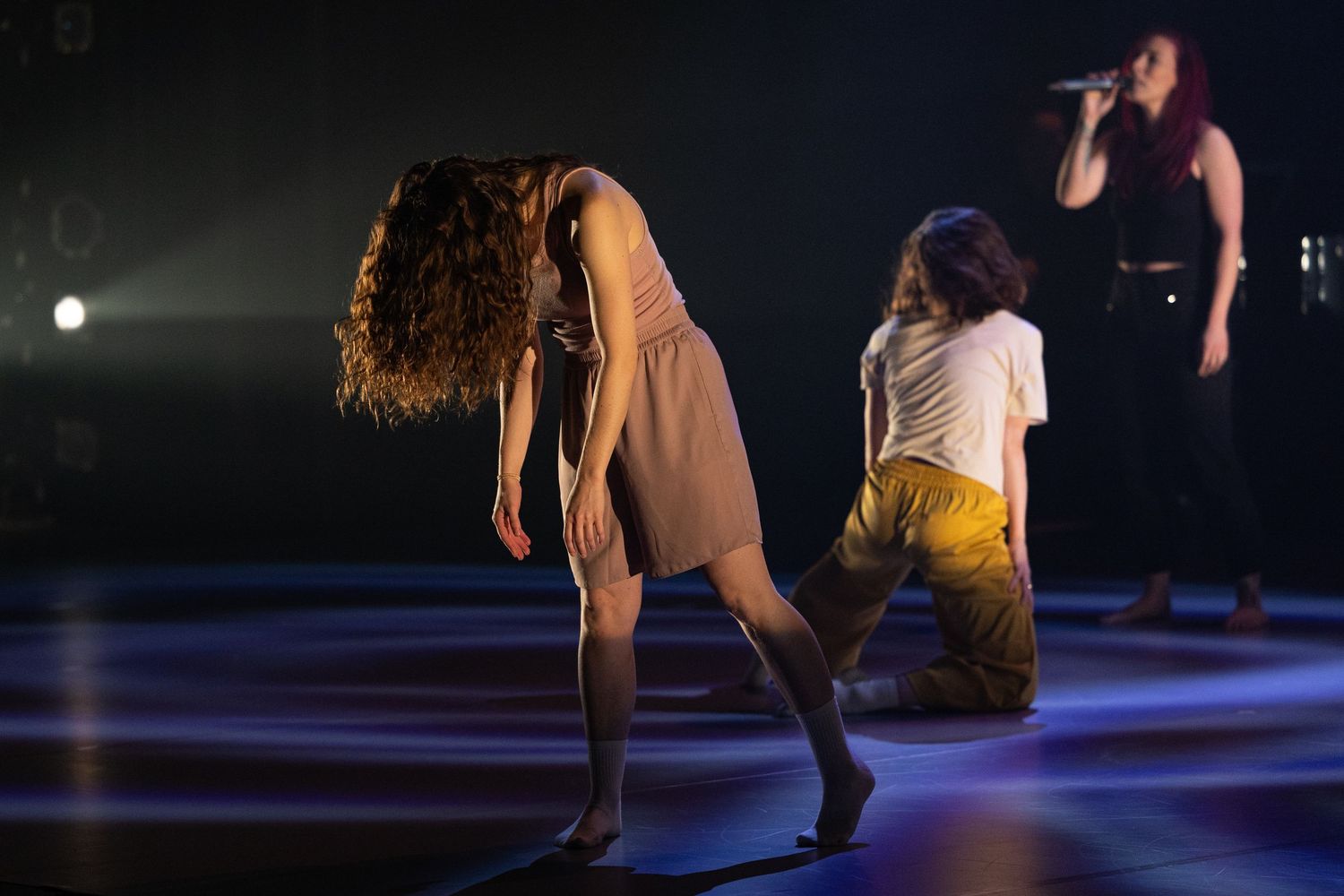 Dancers perform on a dimly lit stage with dramatic lighting against a dark background.