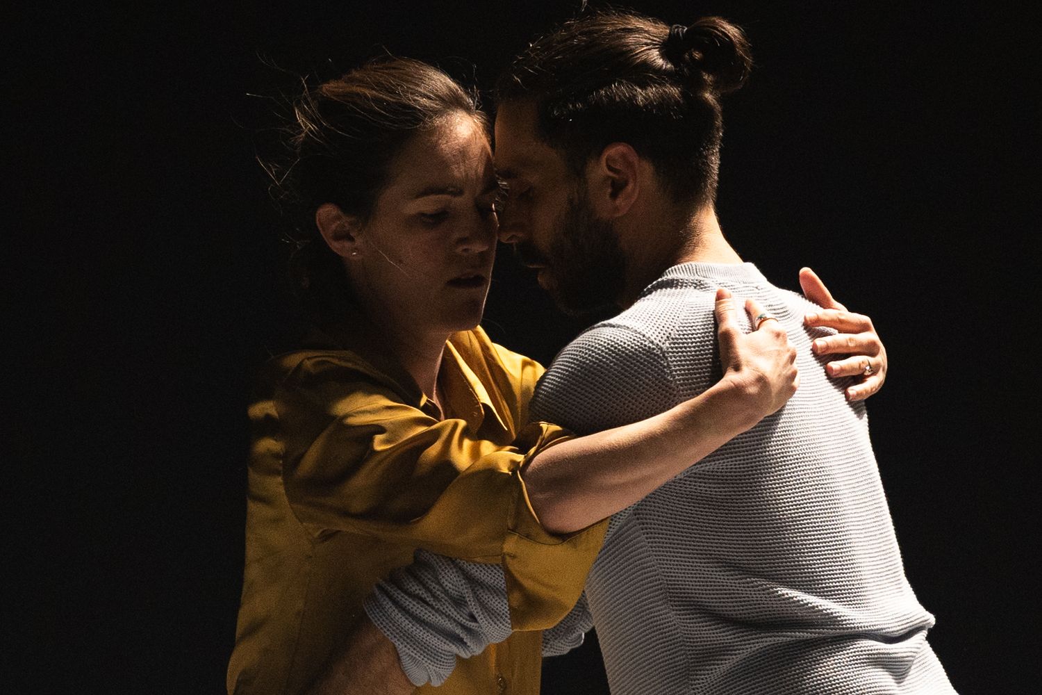 Two dancers perform an intimate partner dance together in dramatic lighting with yellow and dark tones.
