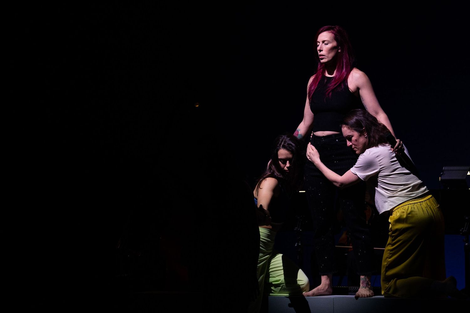 Two performers on a dark stage during a theater performance, one lifted in an acrobatic pose by the other.