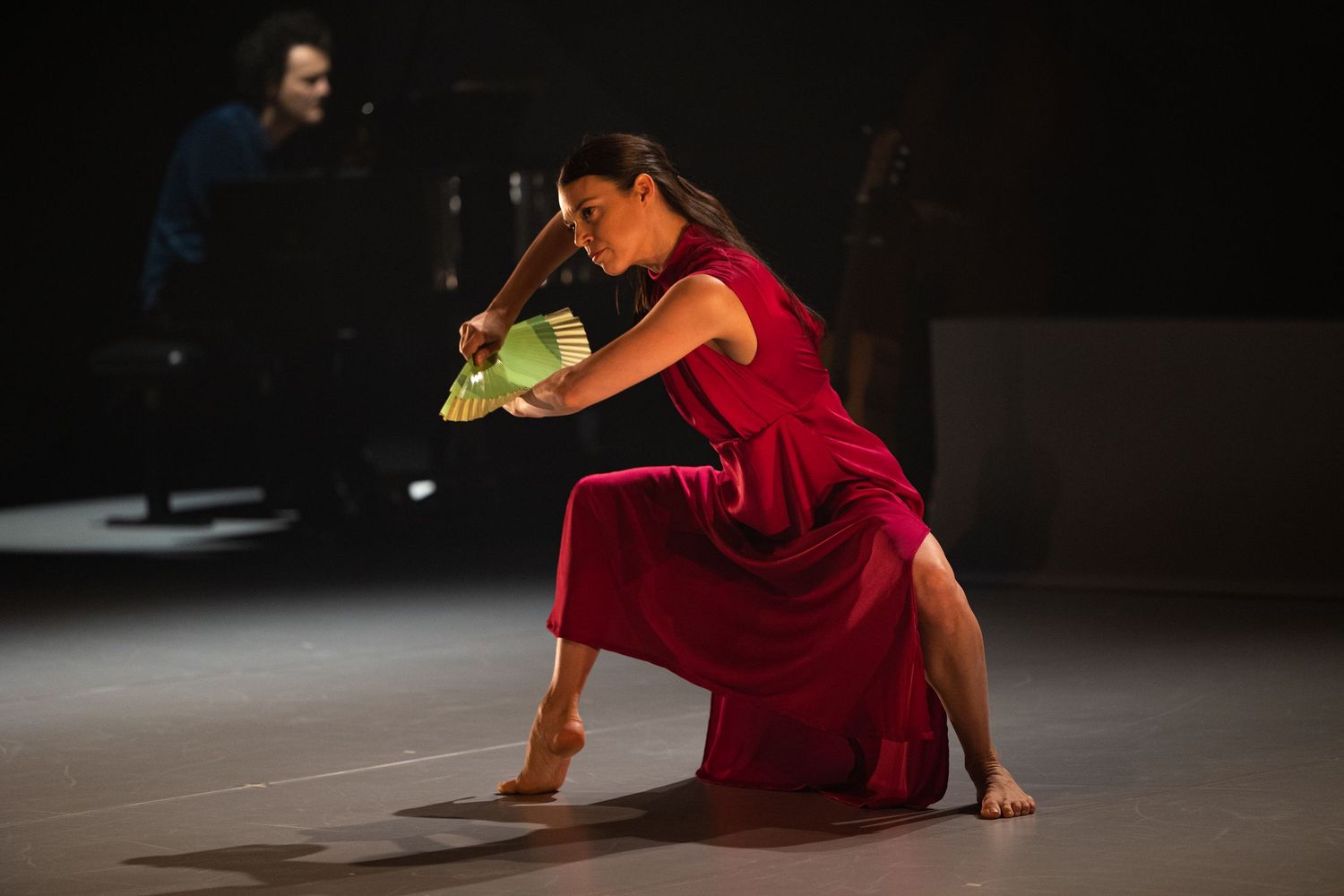 Dancer in red dress performs contemporary dance movement sequence on dark stage.