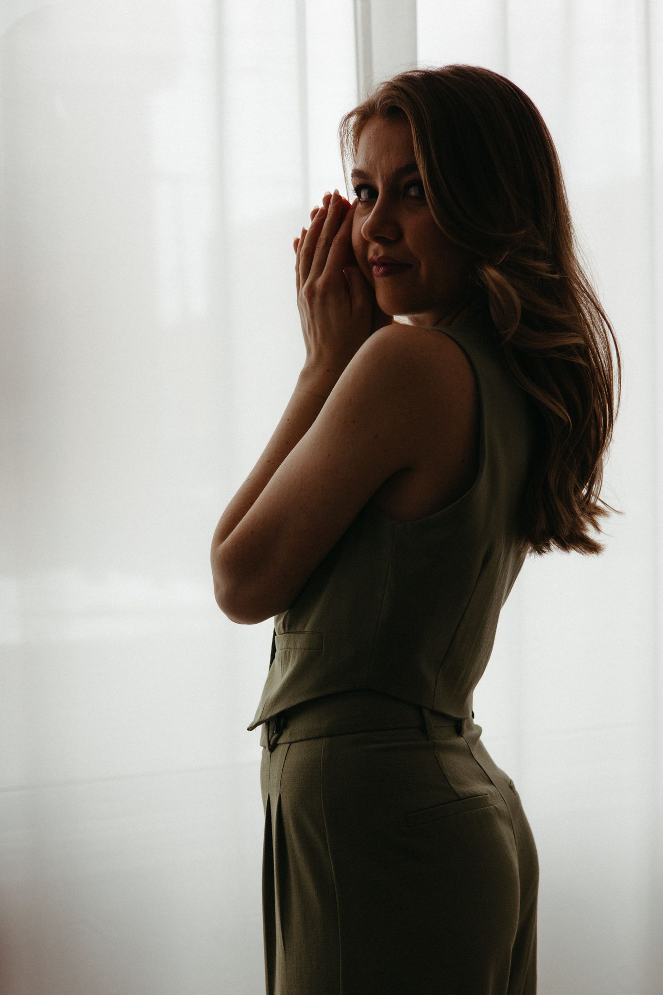 A silhouetted figure in a dark room stands against white curtains creating a moody atmospheric series of poses.