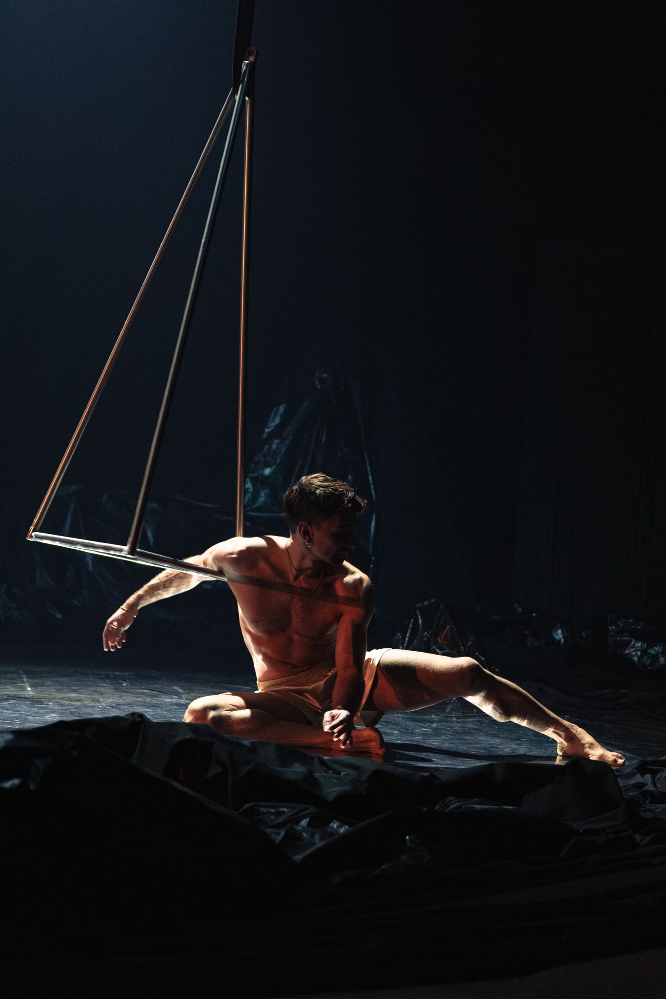 Aerial performer silhouetted against dark backdrop executes graceful suspended movements in dramatic lighting sequence.