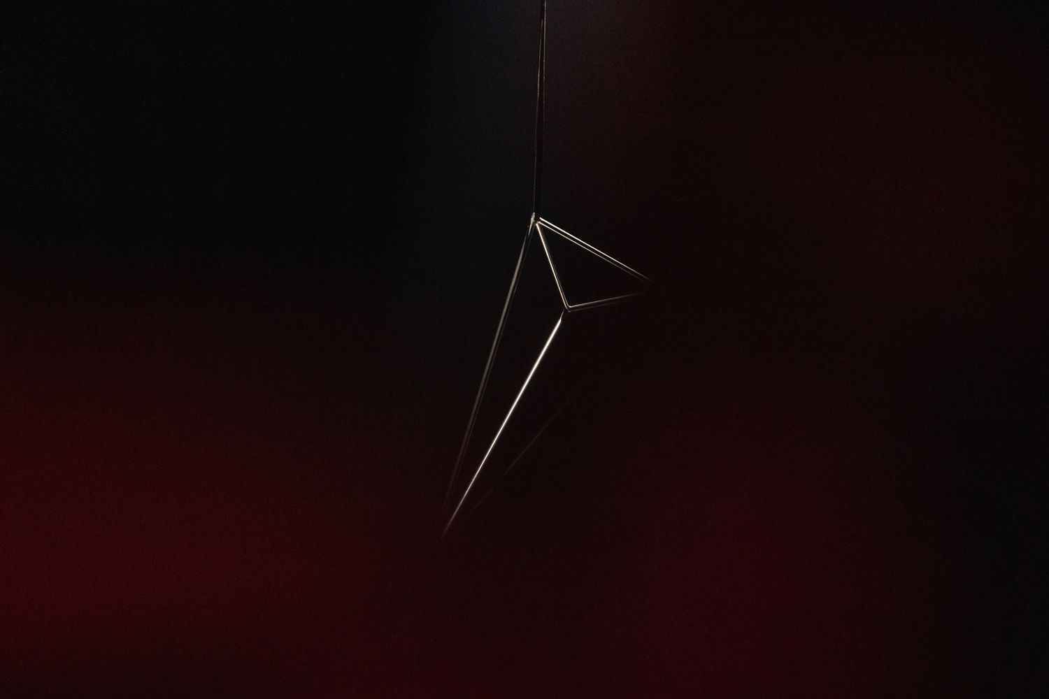 A minimalist wireframe triangle shape floating against a dark red and black gradient background.