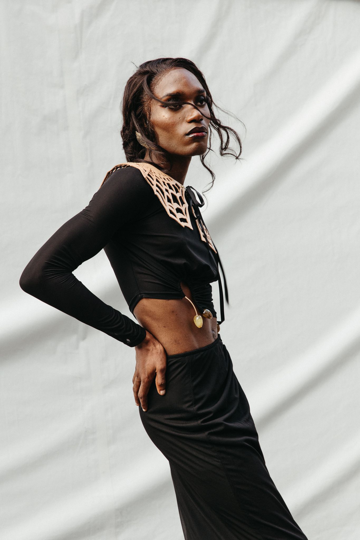 Striking fashion photo of a model in a black crop top with cutout collar detail and matching skirt against white backdrop.
