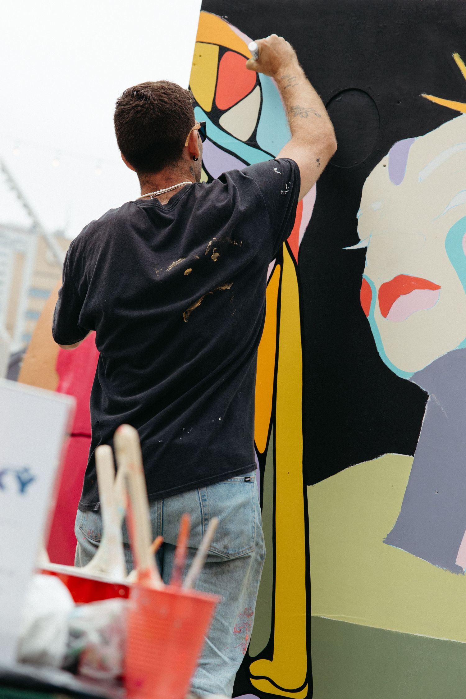 Artist in black hoodie uses spray paint to create colorful street art mural on black wall.