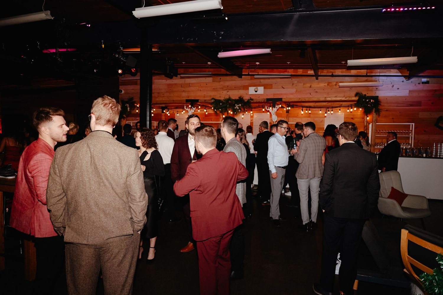 A crowd of people gathered at an indoor event space with wooden walls and ambient lighting.