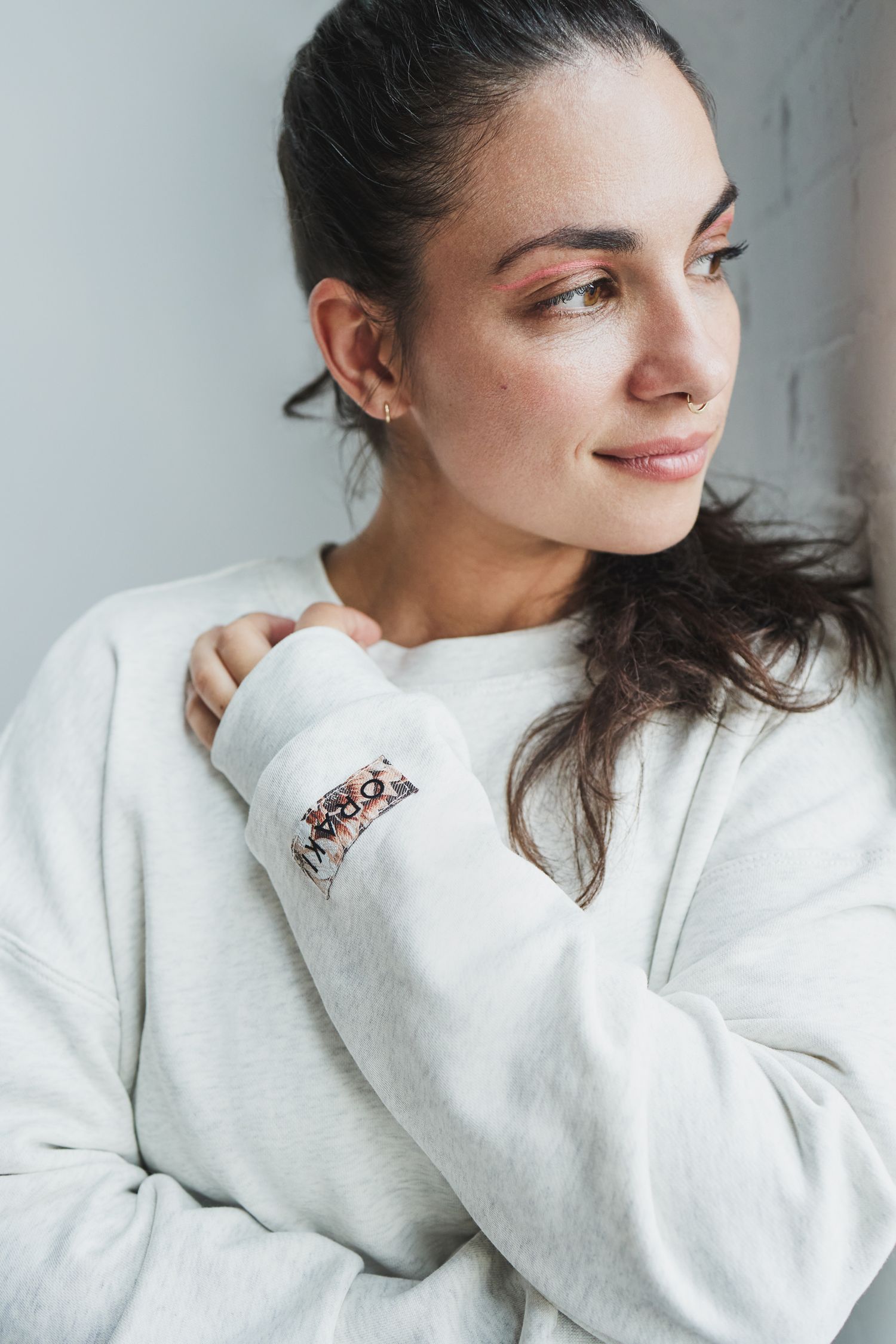 Person in white sweater posing casually against light background.