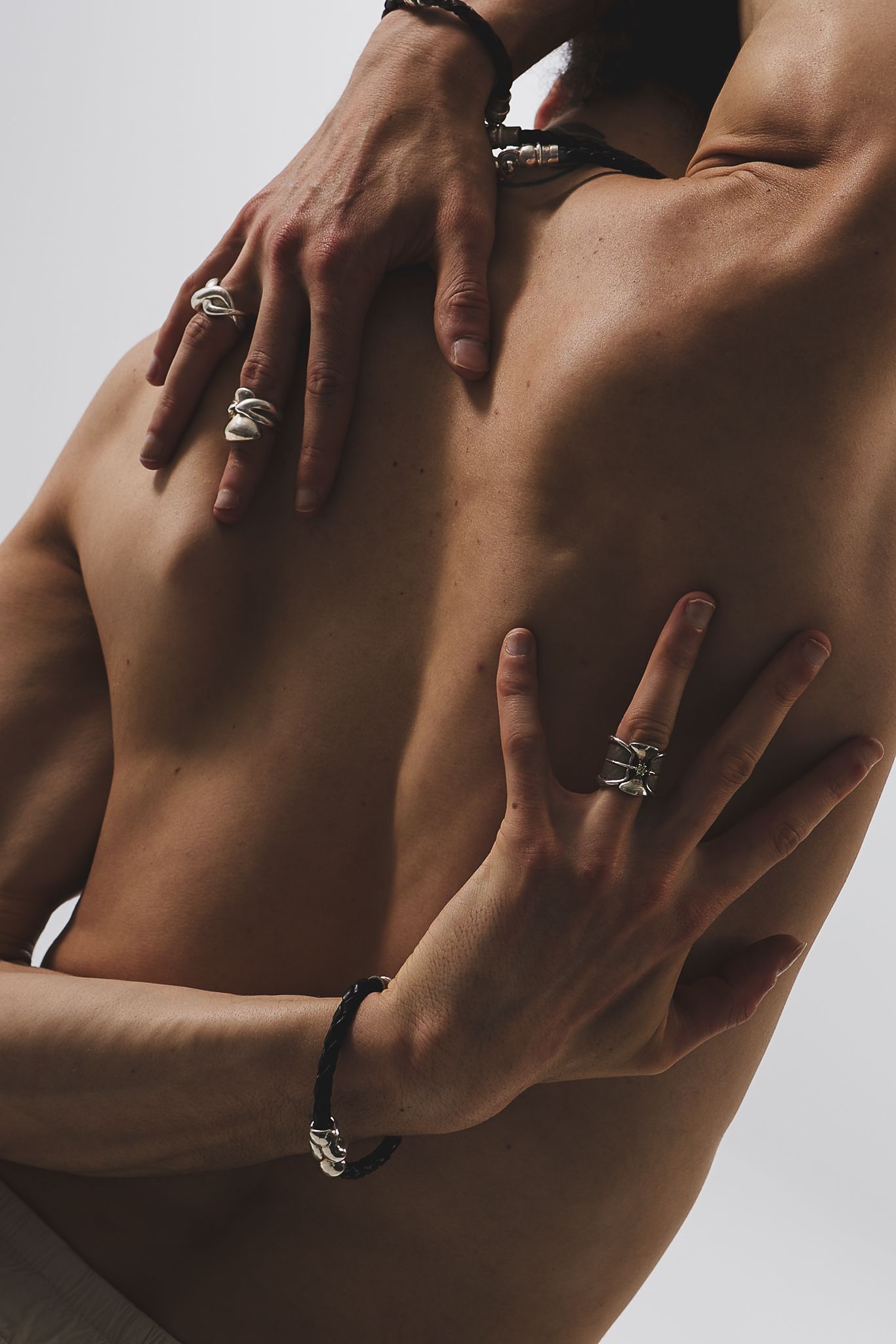 Artistic close-up photograph of hands adorned with multiple silver rings against bare skin in dramatic lighting.