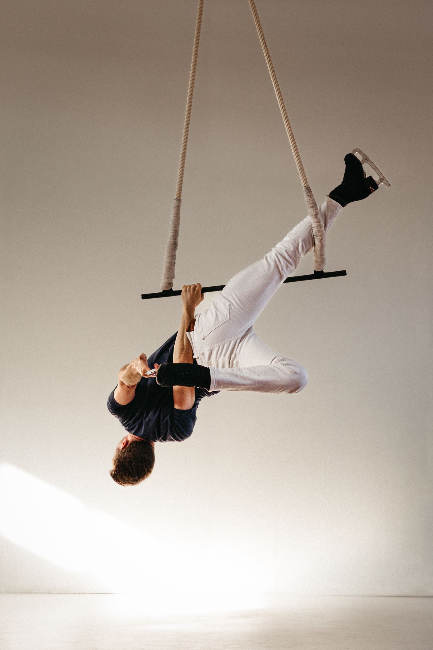 Aerial performer in black and white attire hangs upside down from a trapeze bar against a neutral background.