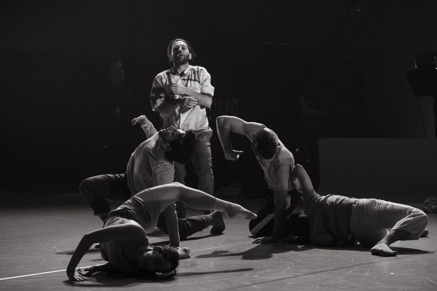 Black and white still captures dancers on stage performing a modern floor routine in dramatic lighting.