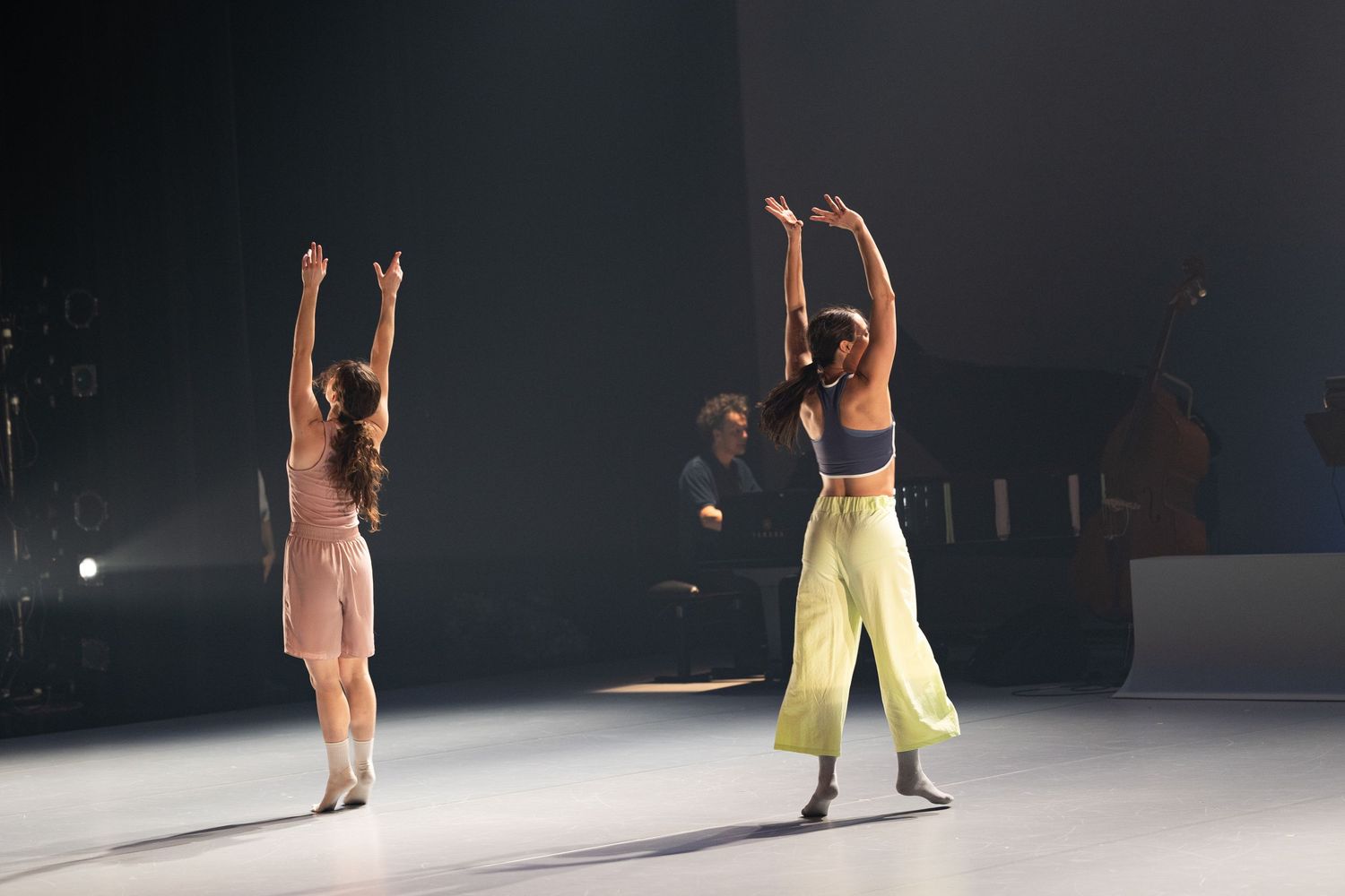 Two dancers perform a contemporary duet on a dark stage with dramatic lighting.