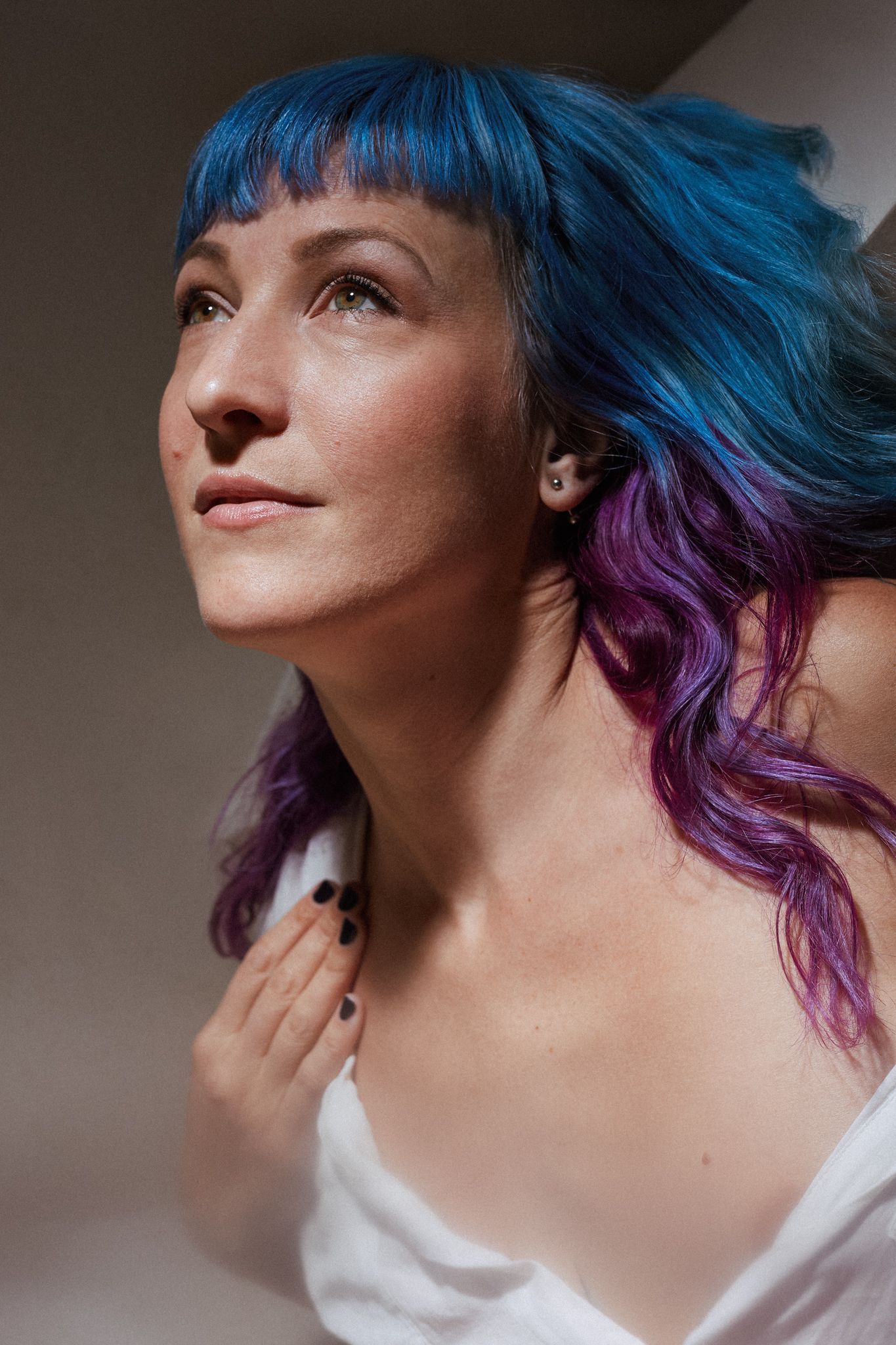 Portrait showing vibrant blue and purple dyed hair styled in waves against a neutral background.