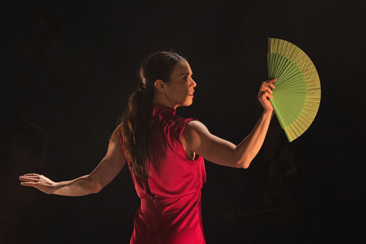 A dancer in a red dress performs with a yellow fan against a dark background, creating dramatic contrast and motion.