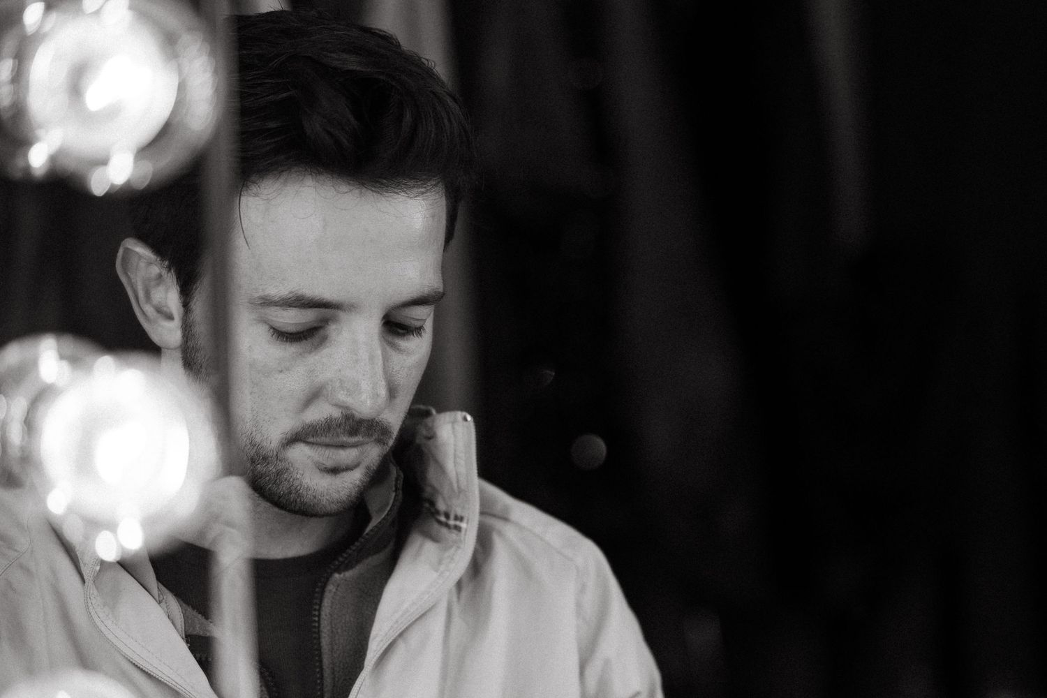 Black and white portrait of a man looking down thoughtfully in a white shirt with soft bokeh lights in the background.