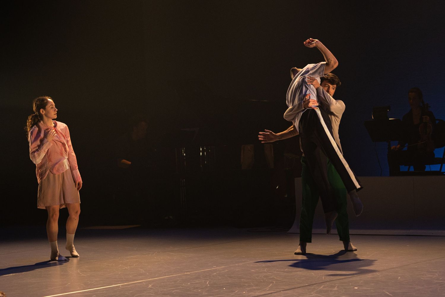 Contemporary dancers perform an expressive sequence in a dimly lit theater space.