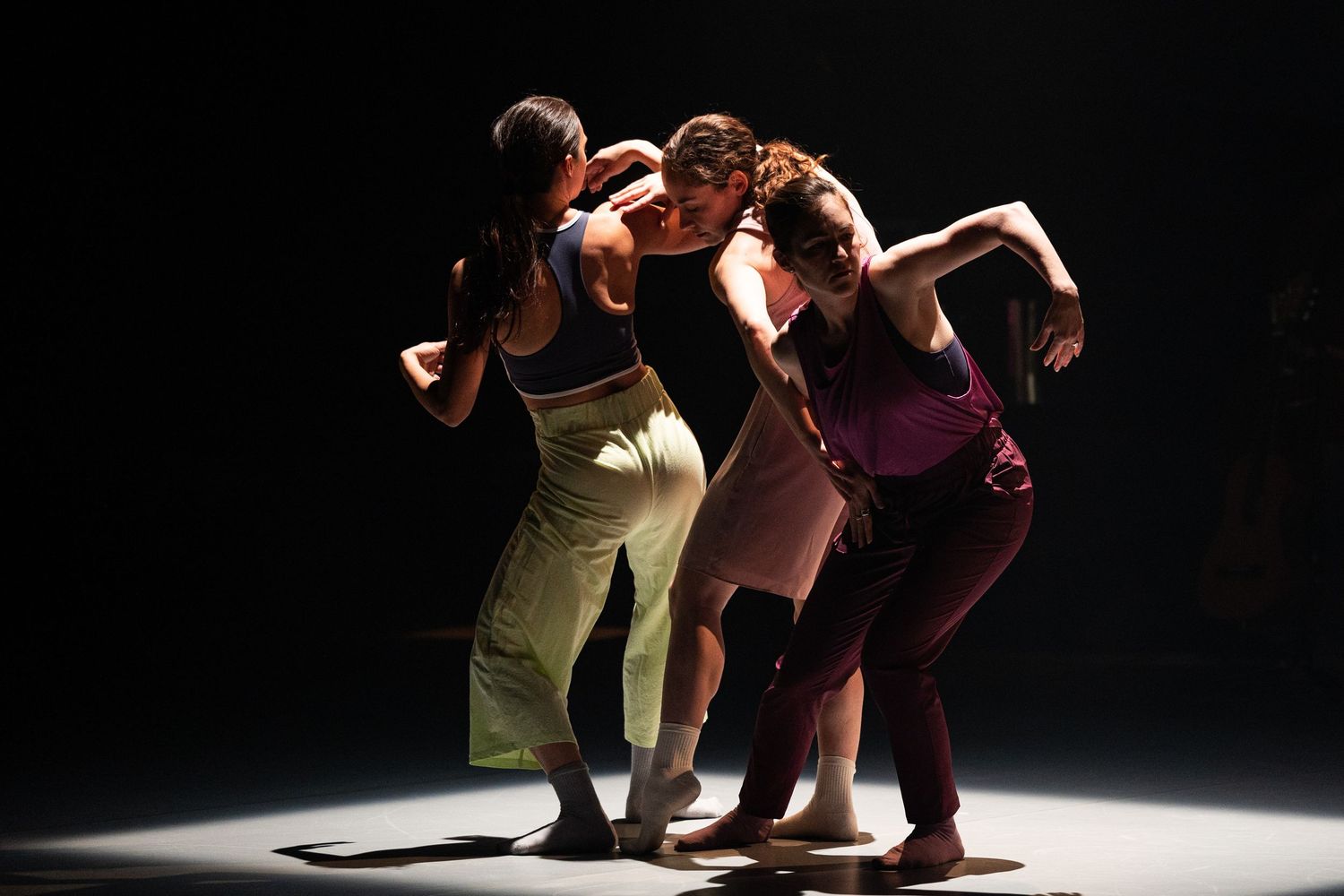 Modern dancers perform dramatic choreography in silhouette against a dark stage with dramatic spotlighting.