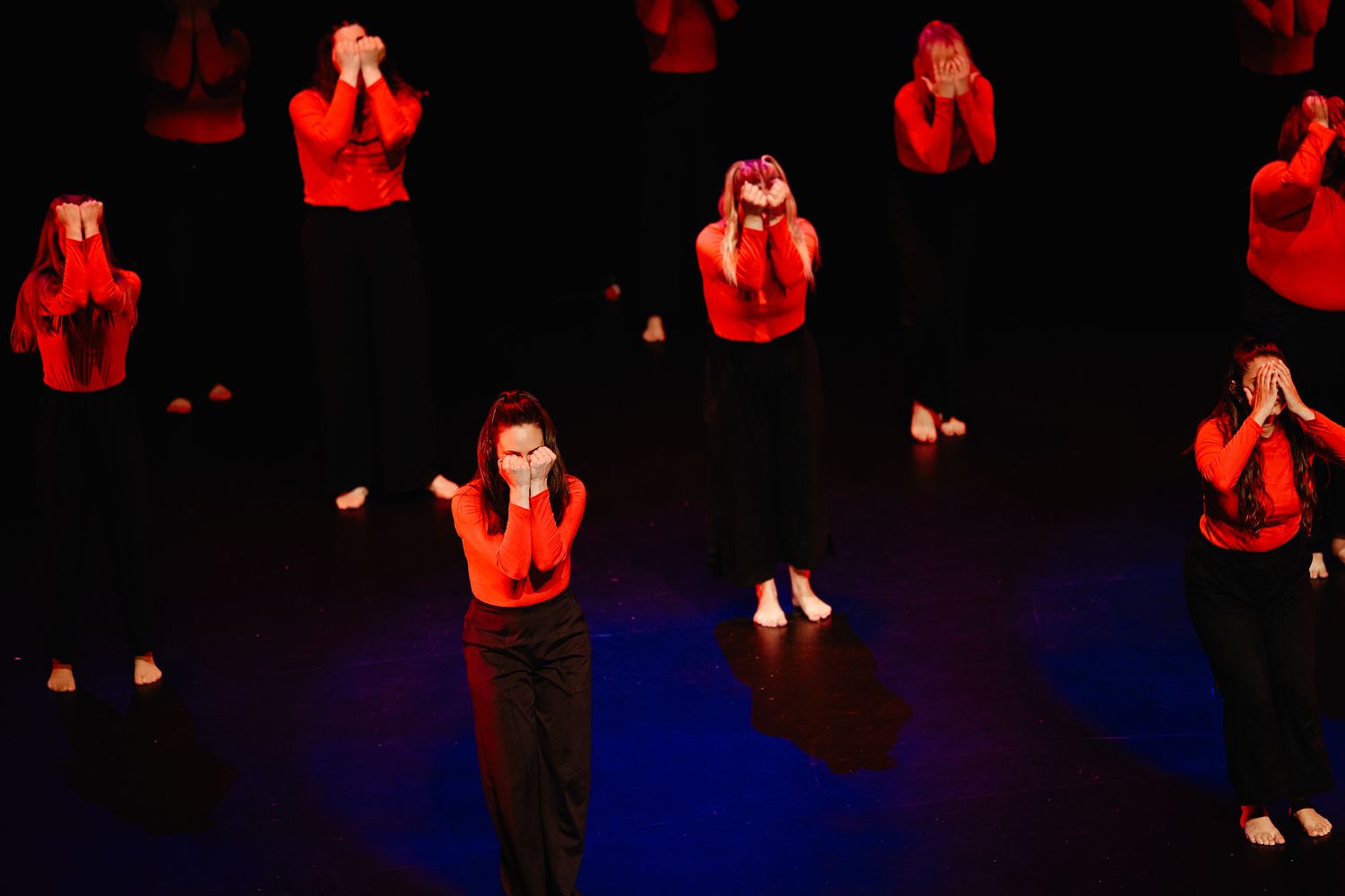 A stage performance shows people dancing in dramatic lighting with red and blue colors casting dramatic shadows.