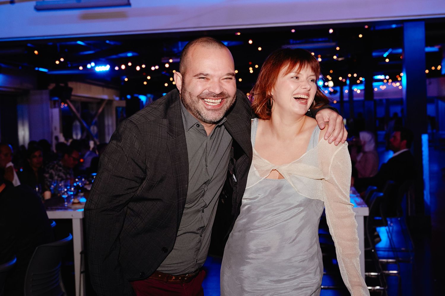 People enjoying themselves at a dimly lit event venue with blue ambient lighting in the background.
