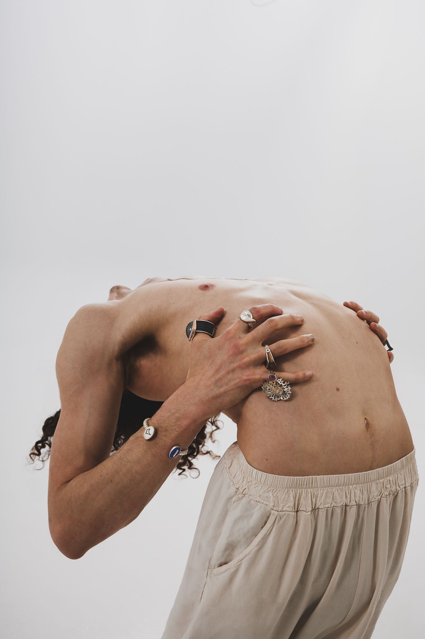 An artistic nude portrait shows a person arching backward with hands against their torso against a light gray background.