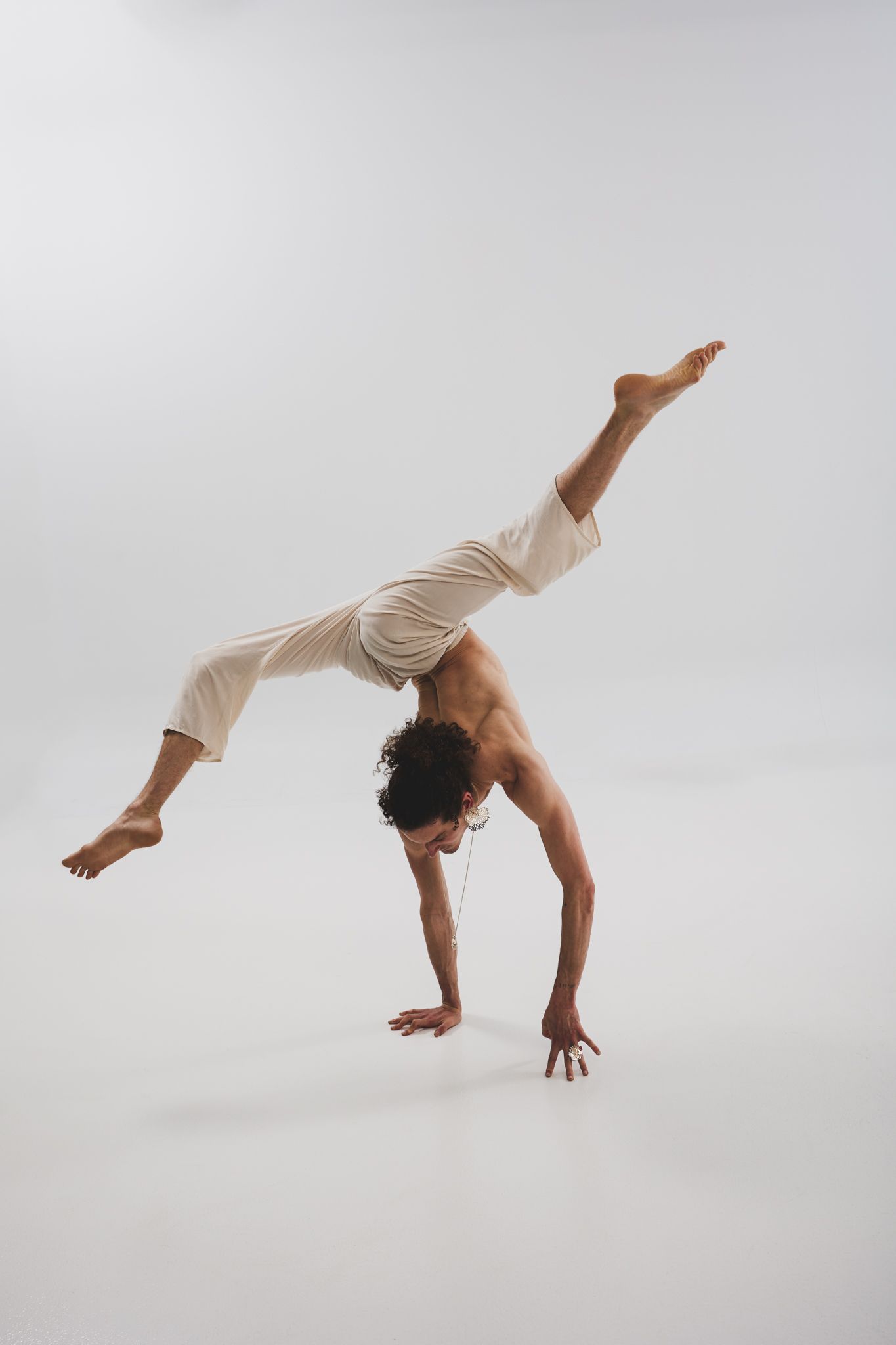 Modern dancer in light attire demonstrates fluid movements and aerial poses on white background.