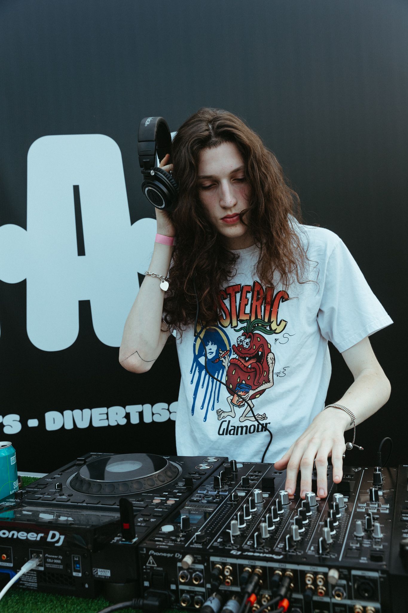 DJ mixing tracks on a professional controller deck with hands adjusting controls in a dimly lit environment.