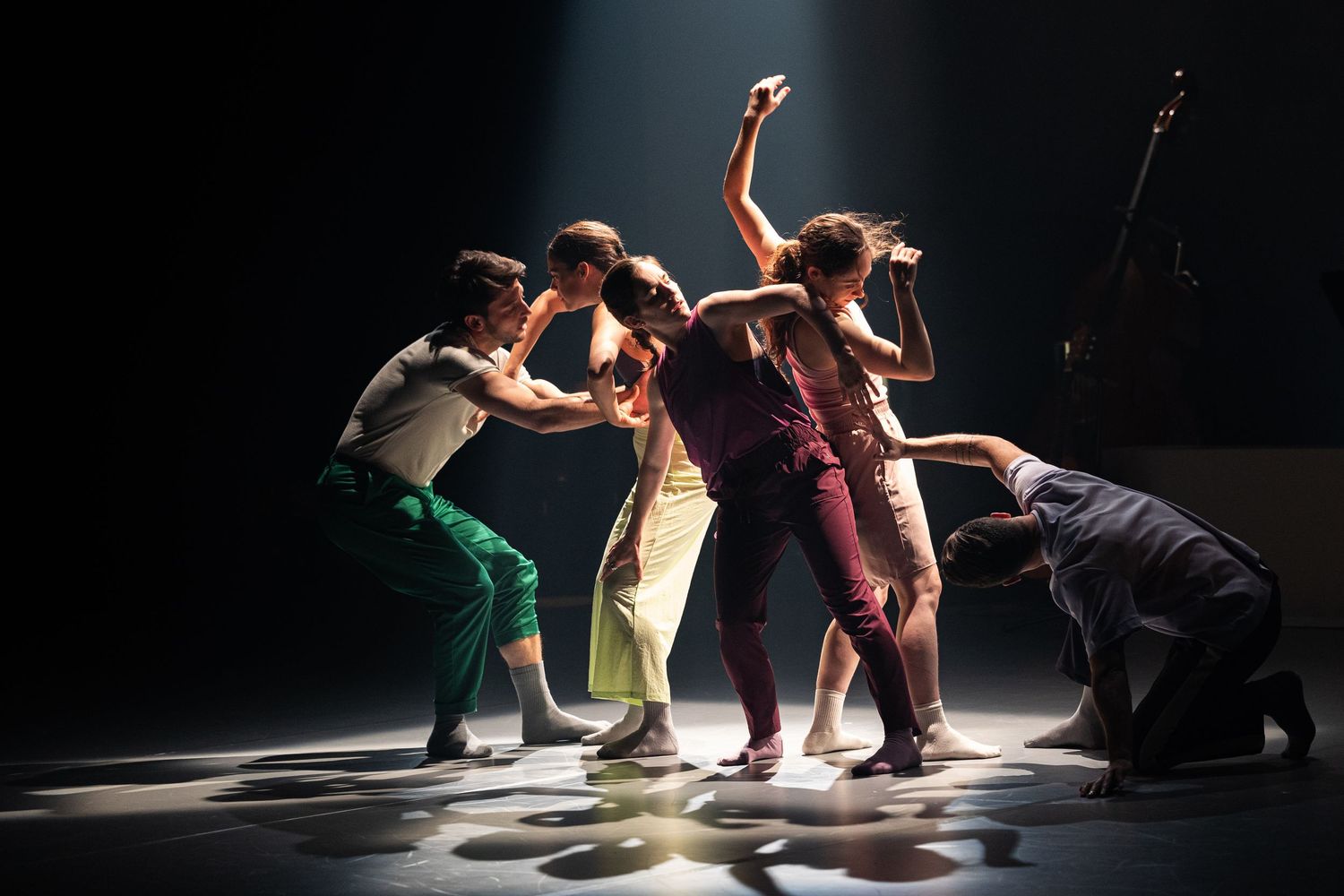 Contemporary dancers performing dynamic floor movements in a darkly lit theater space during a modern dance performance.