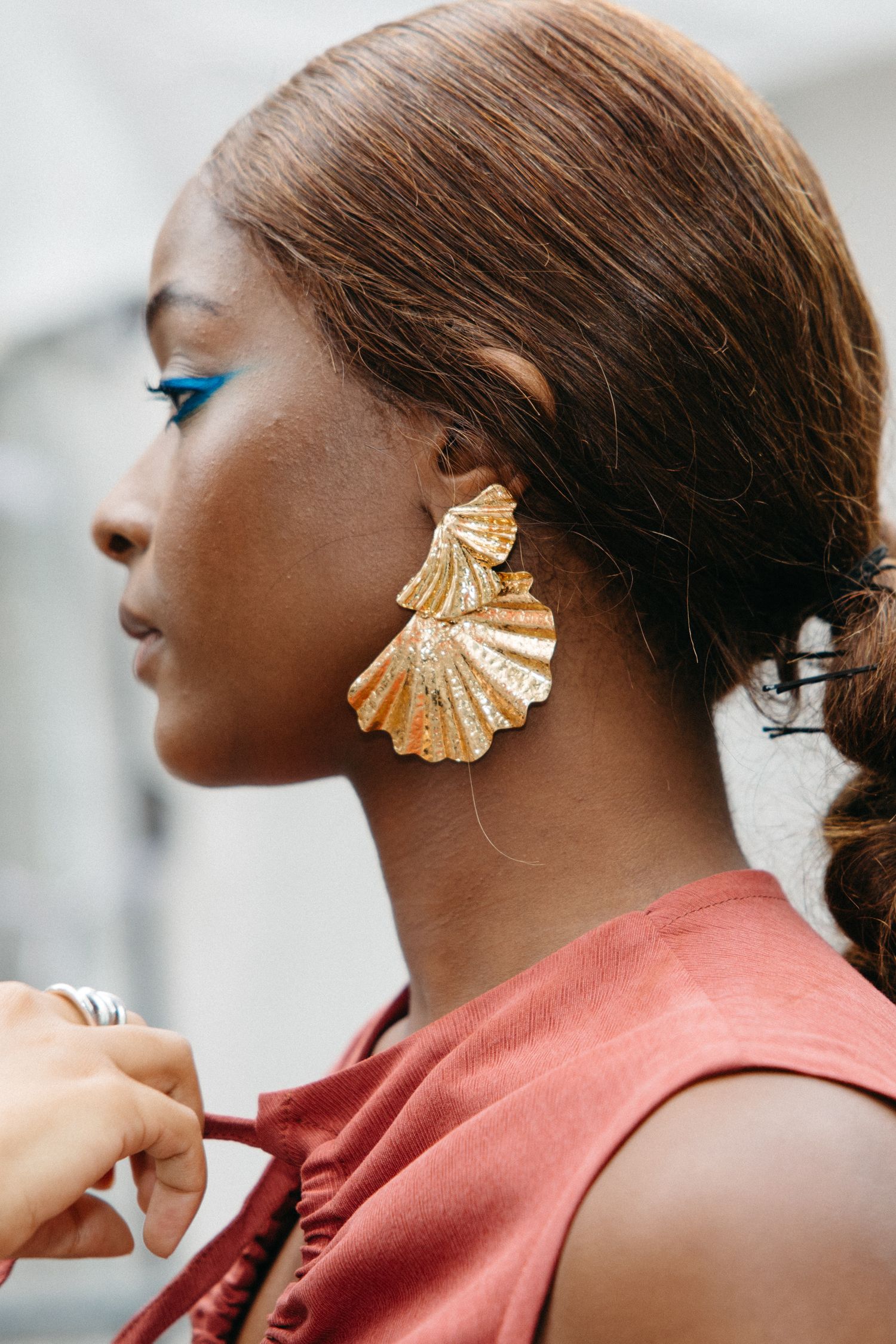 Close-up profile view of a person wearing a striking gold seashell-shaped statement earring against a light background.