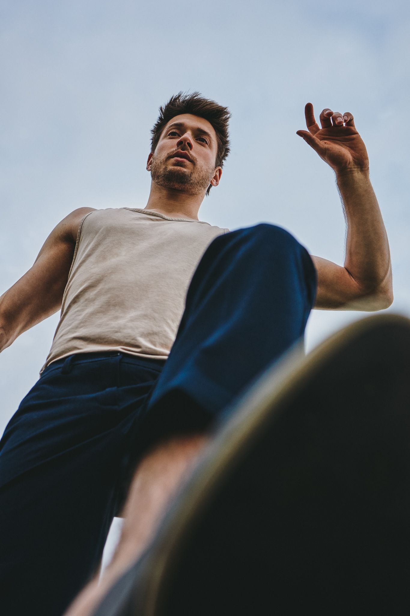 Low angle sequence of someone in a gray tank top and dark pants against a blue sky making joyful gestures.