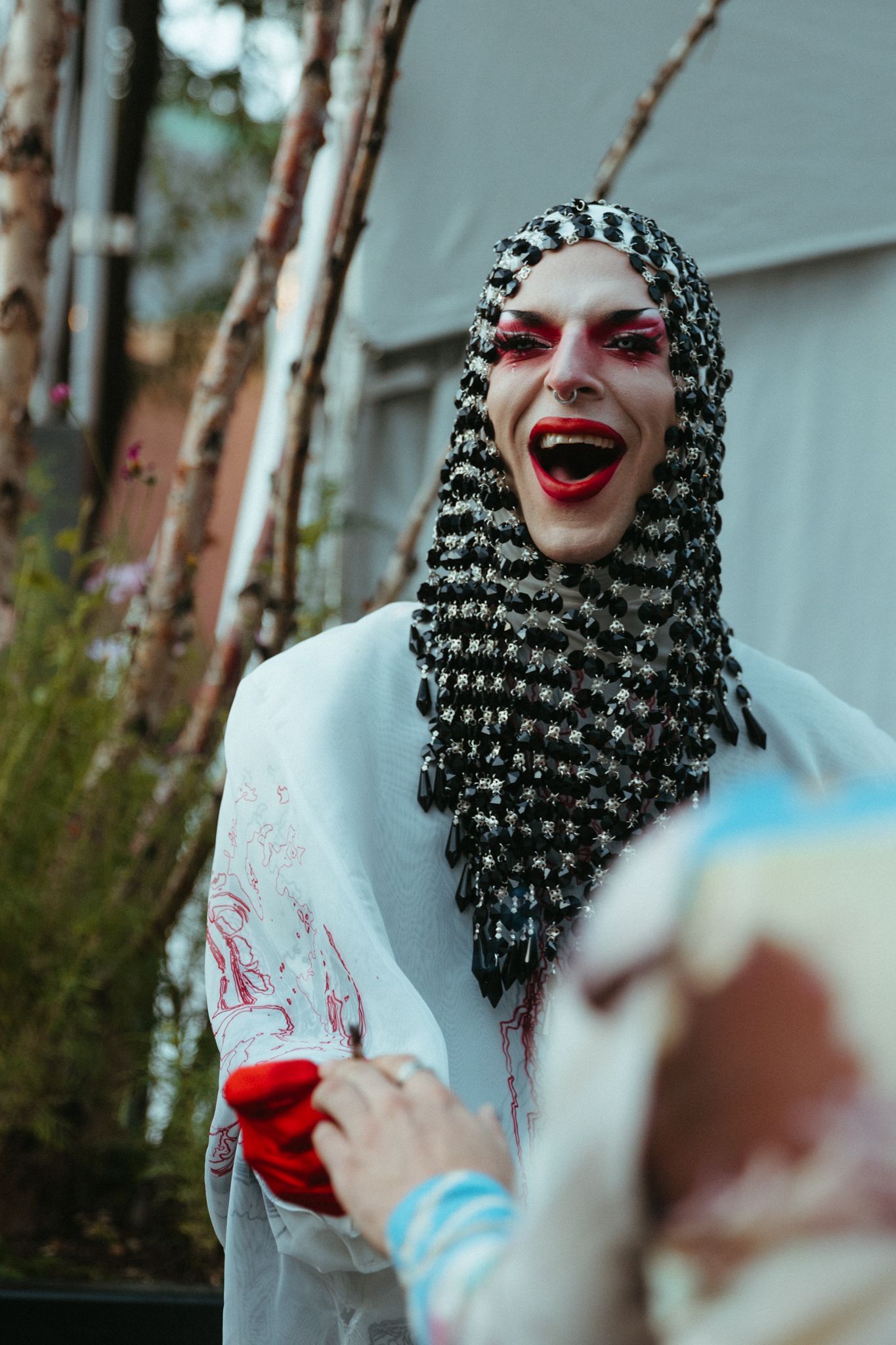 Four sequential images show someone in white attire and a patterned headdress laughing outdoors among trees.