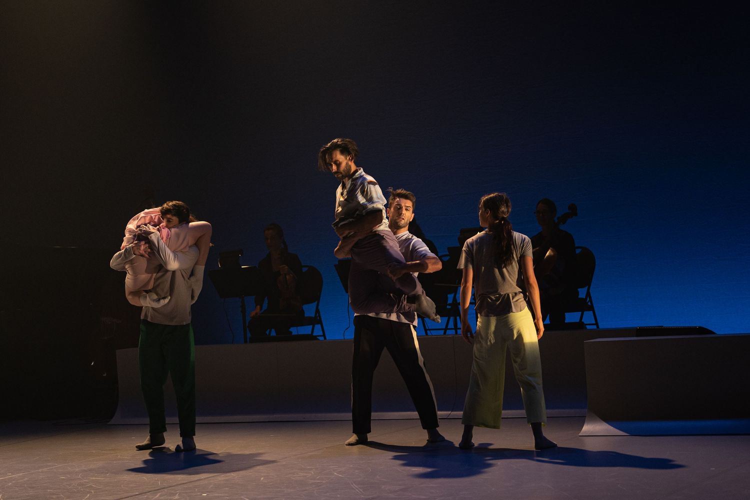 Performers create dynamic silhouettes against a dark blue backdrop in this modern dance performance piece.