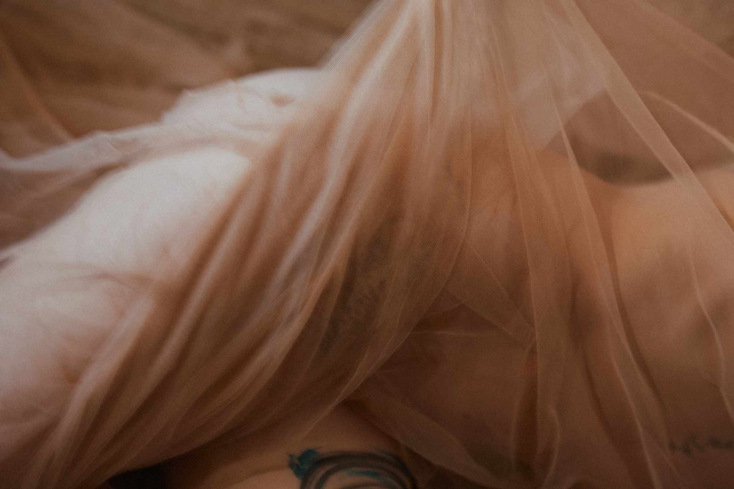 Soft peach-colored tulle fabric creates an ethereal, dreamy texture with delicate folds and translucent layers.