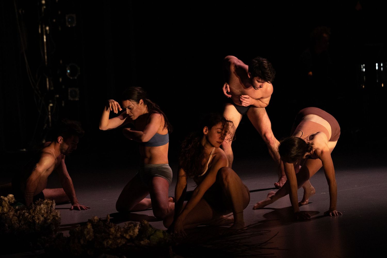 Dramatic dance performance on dark stage showing graceful movements and striking poses in warm lighting.