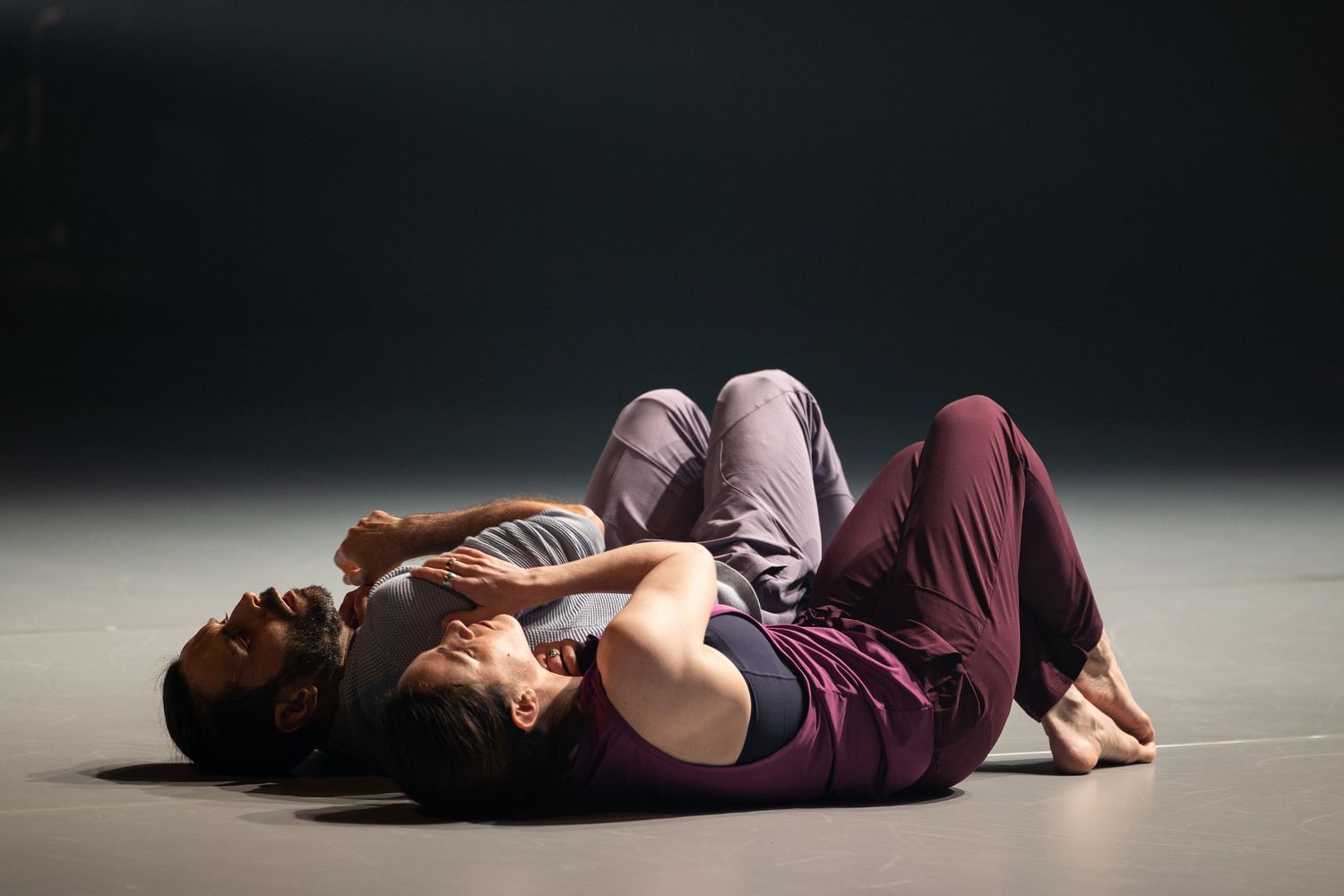 A person wearing a burgundy outfit lies on a dark floor in multiple sequential poses.