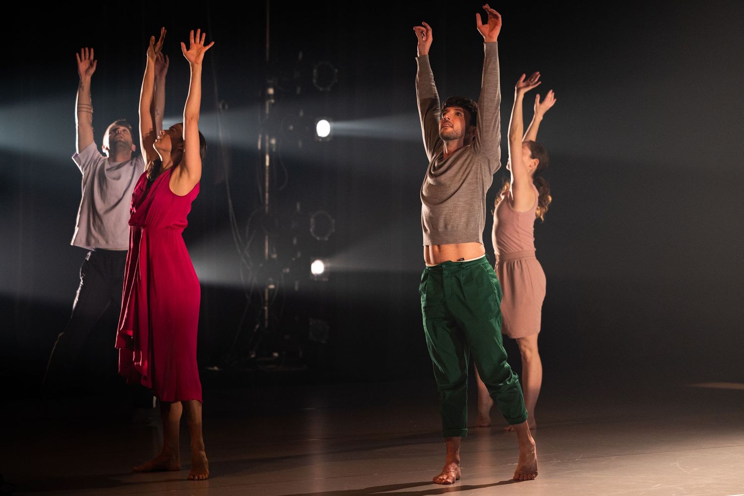 Contemporary dancers perform a dynamic duet in a dark studio space with dramatic spotlight illumination.