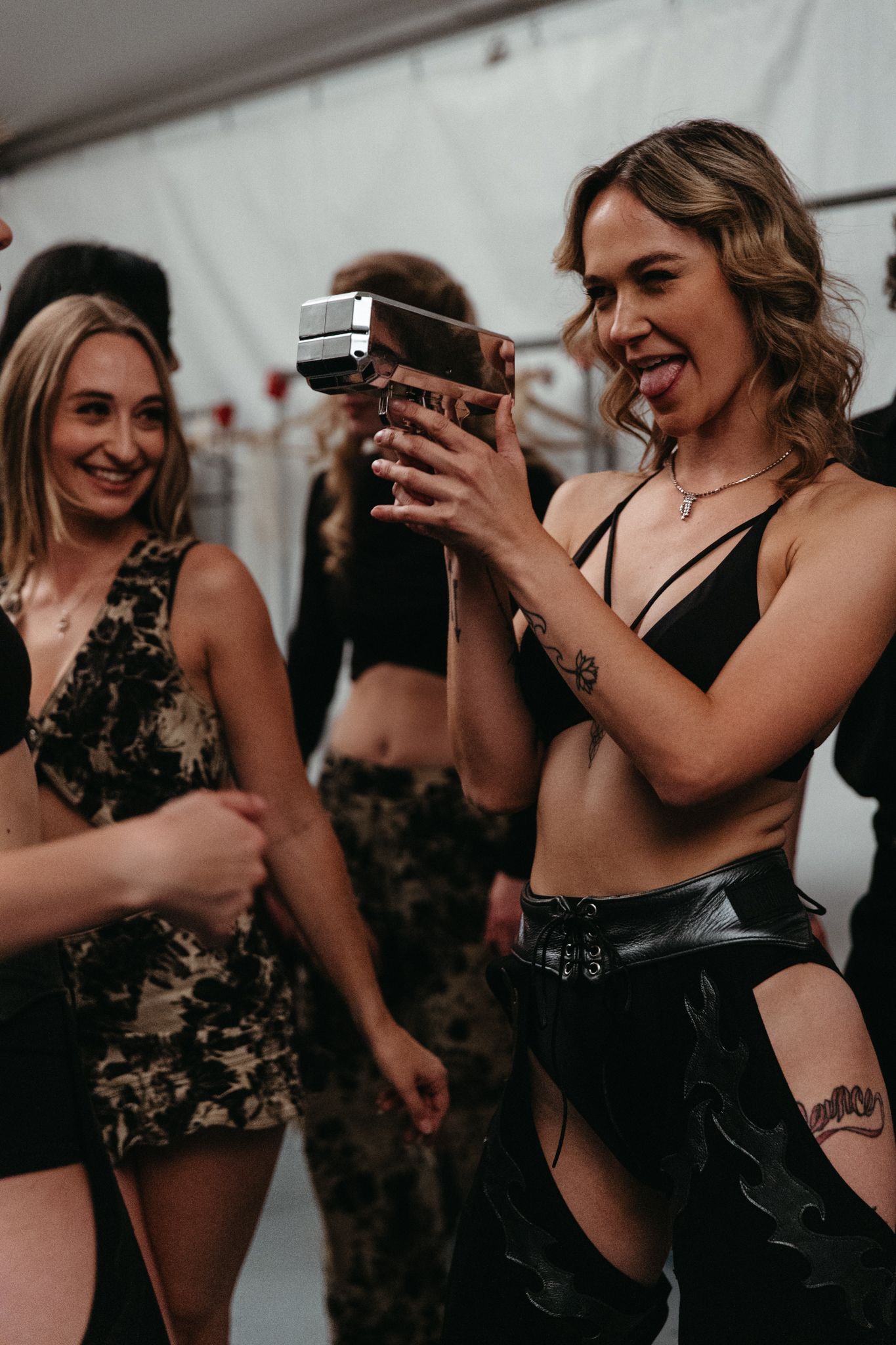 Young women in party attire dance and laugh while holding drinks at a nightclub event.