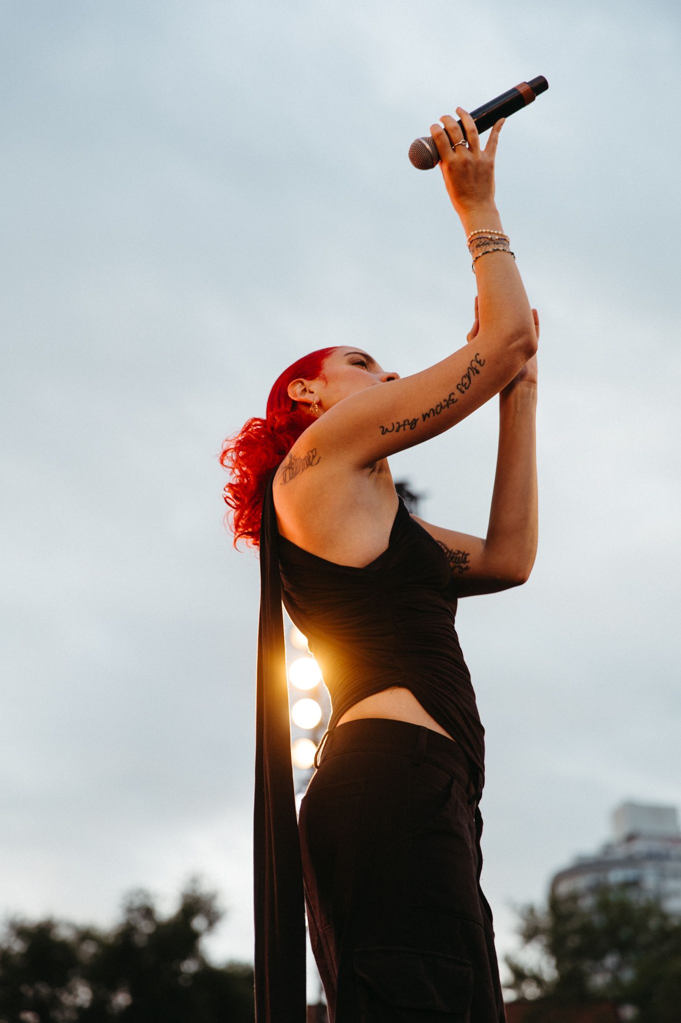 A silhouette performing against a bright sunlit sky wearing a black outfit with red hair details.