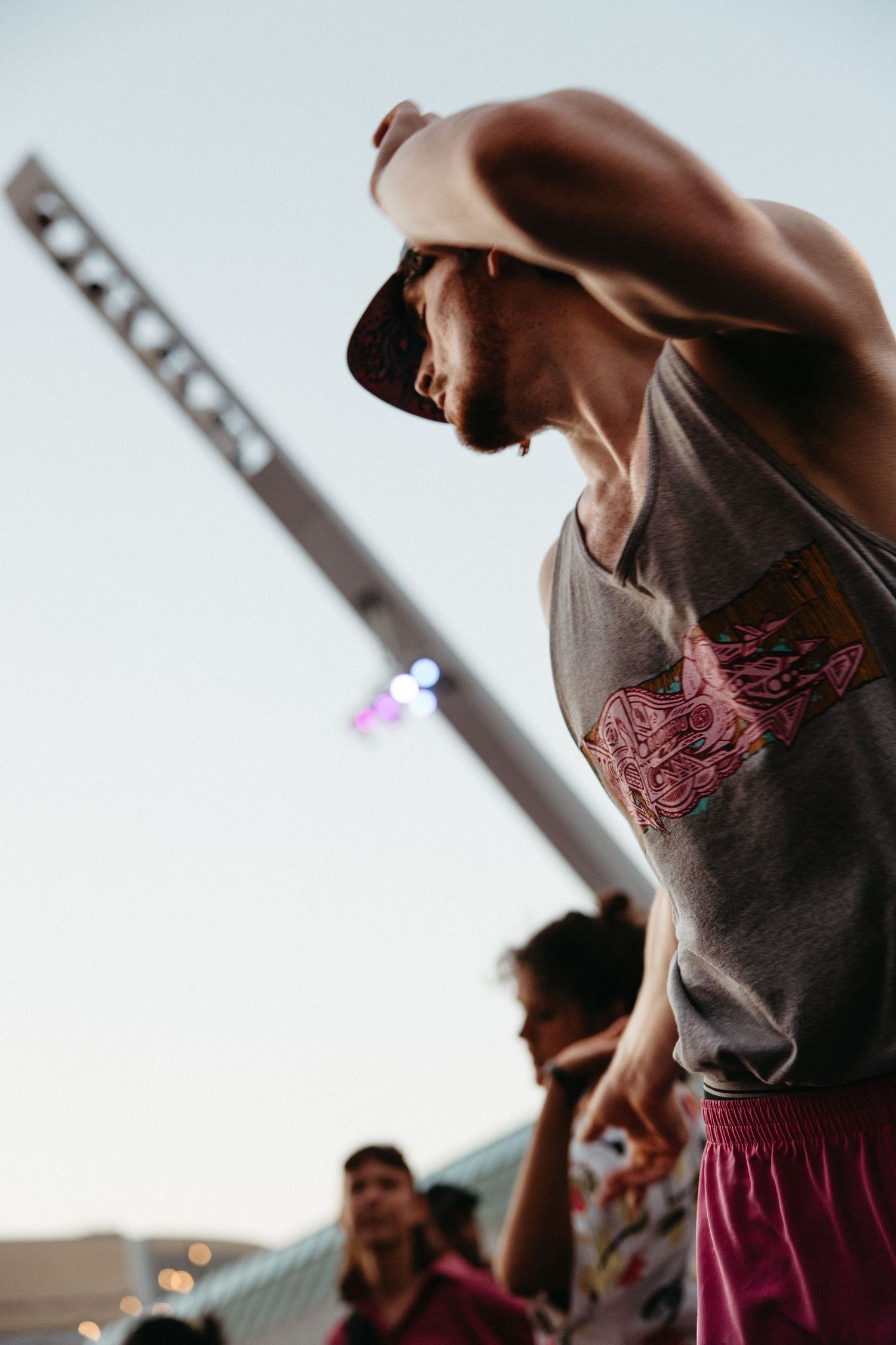 A concertgoer in a gray tank top and red shorts jumps energetically at an outdoor music performance.