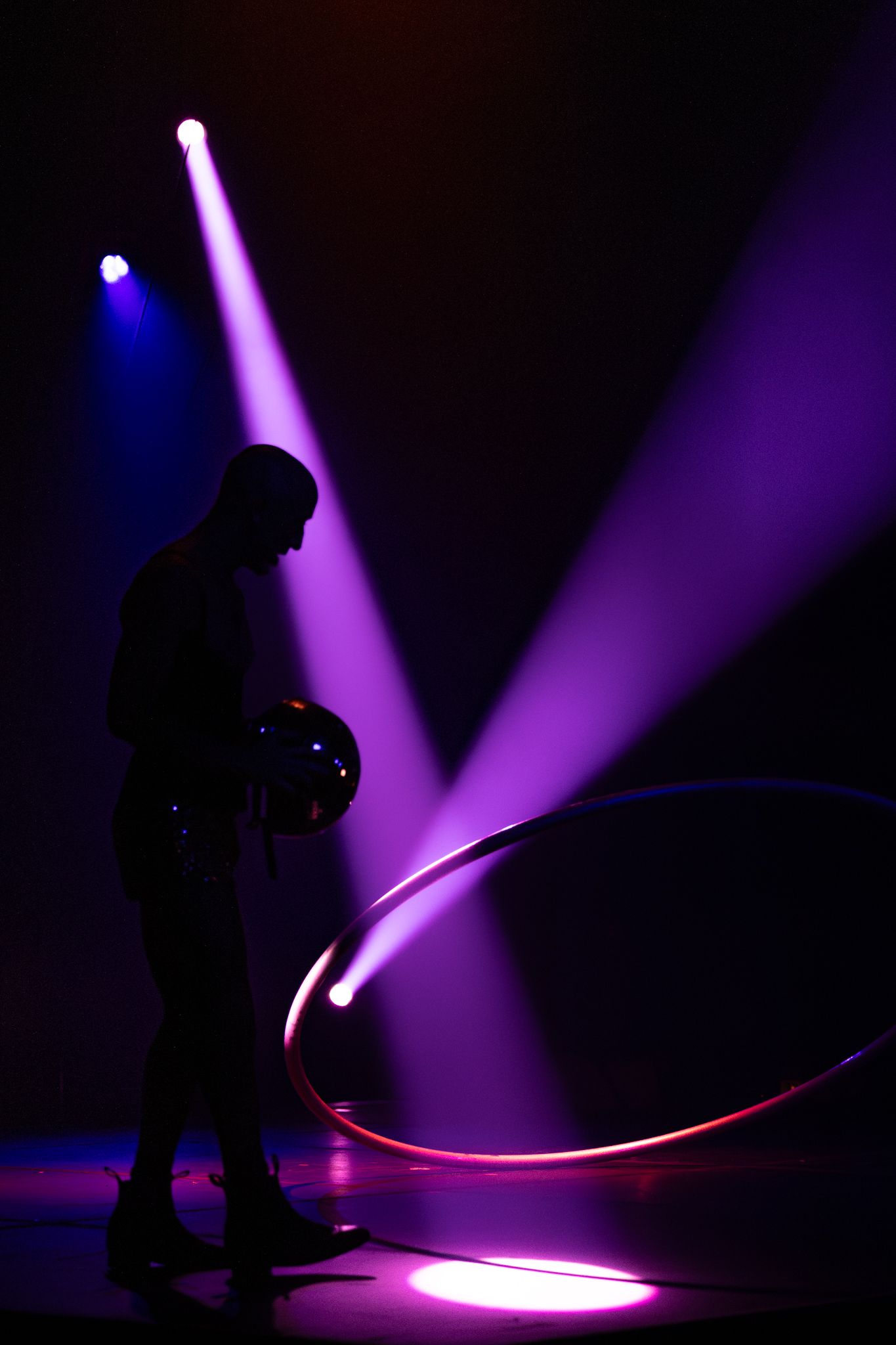 Silhouetted figure performs with illuminated hoop against dramatic purple and blue stage lighting.