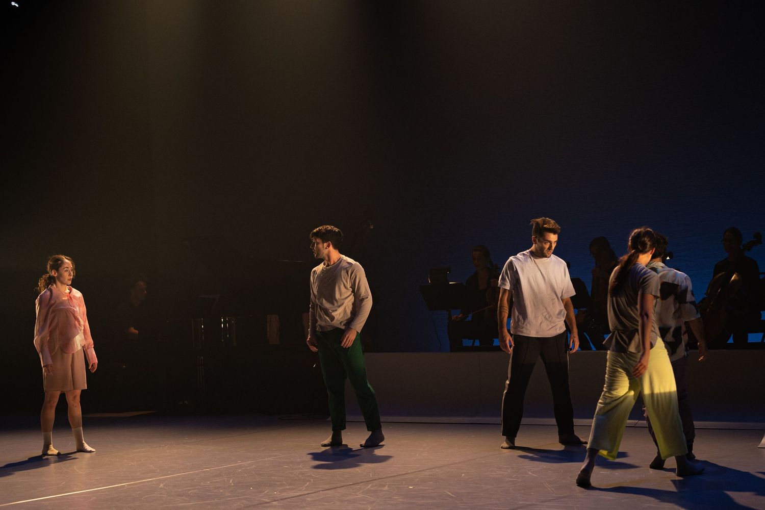 Performers moving across a dark stage in a modern dance performance with dramatic lighting and silhouettes.