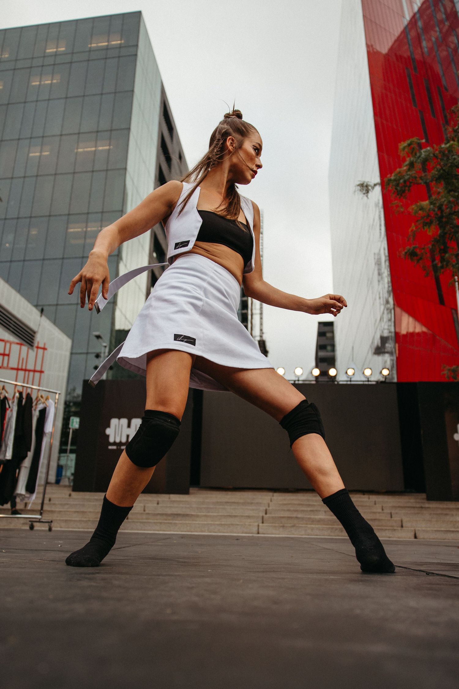 Athletic dancer in sportswear performs dynamic urban dance move against modern city backdrop with colorful buildings.