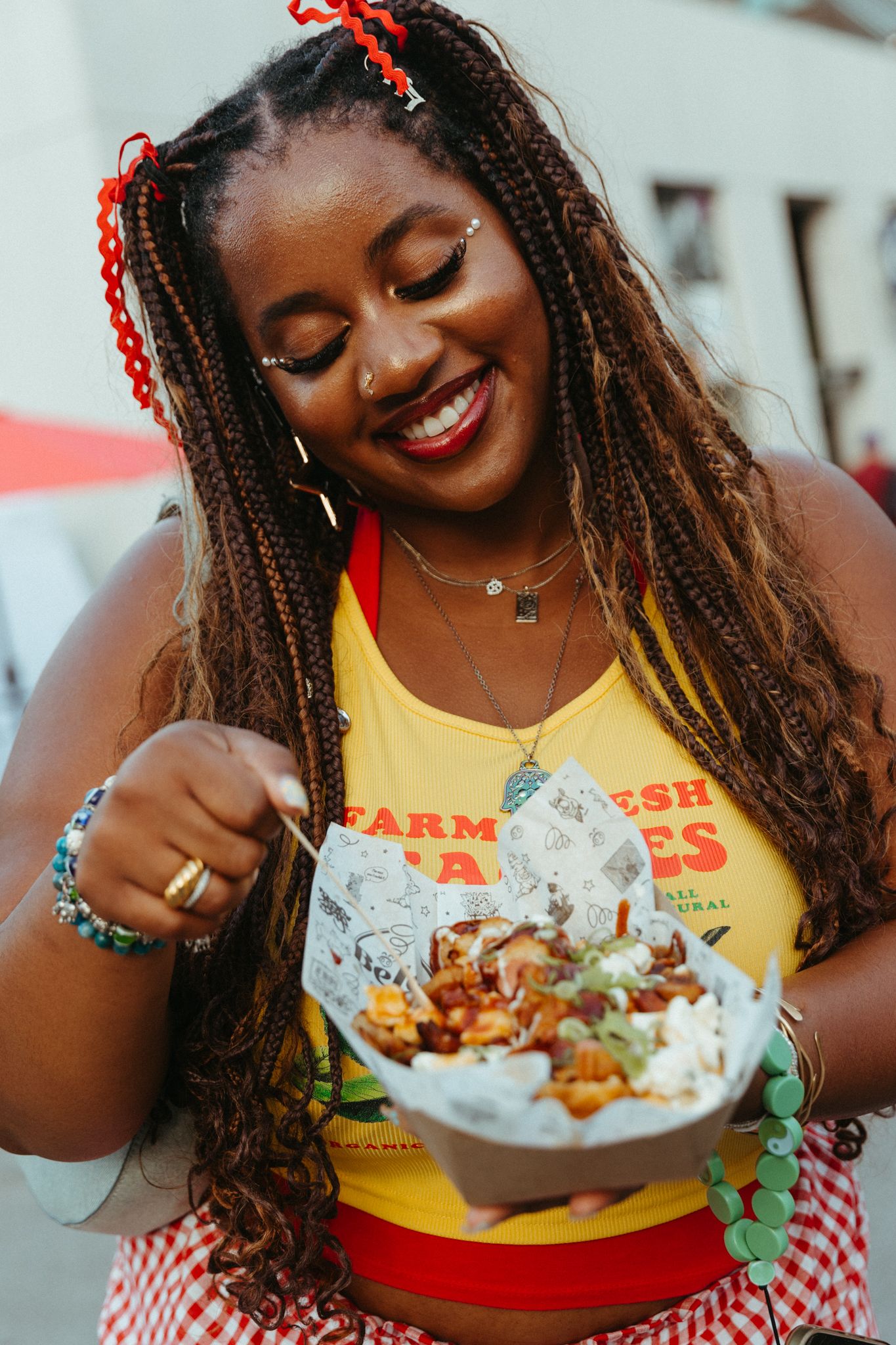 A person in a yellow tank top and red striped skirt enjoys a fresh takeout meal with visible joy and enthusiasm.